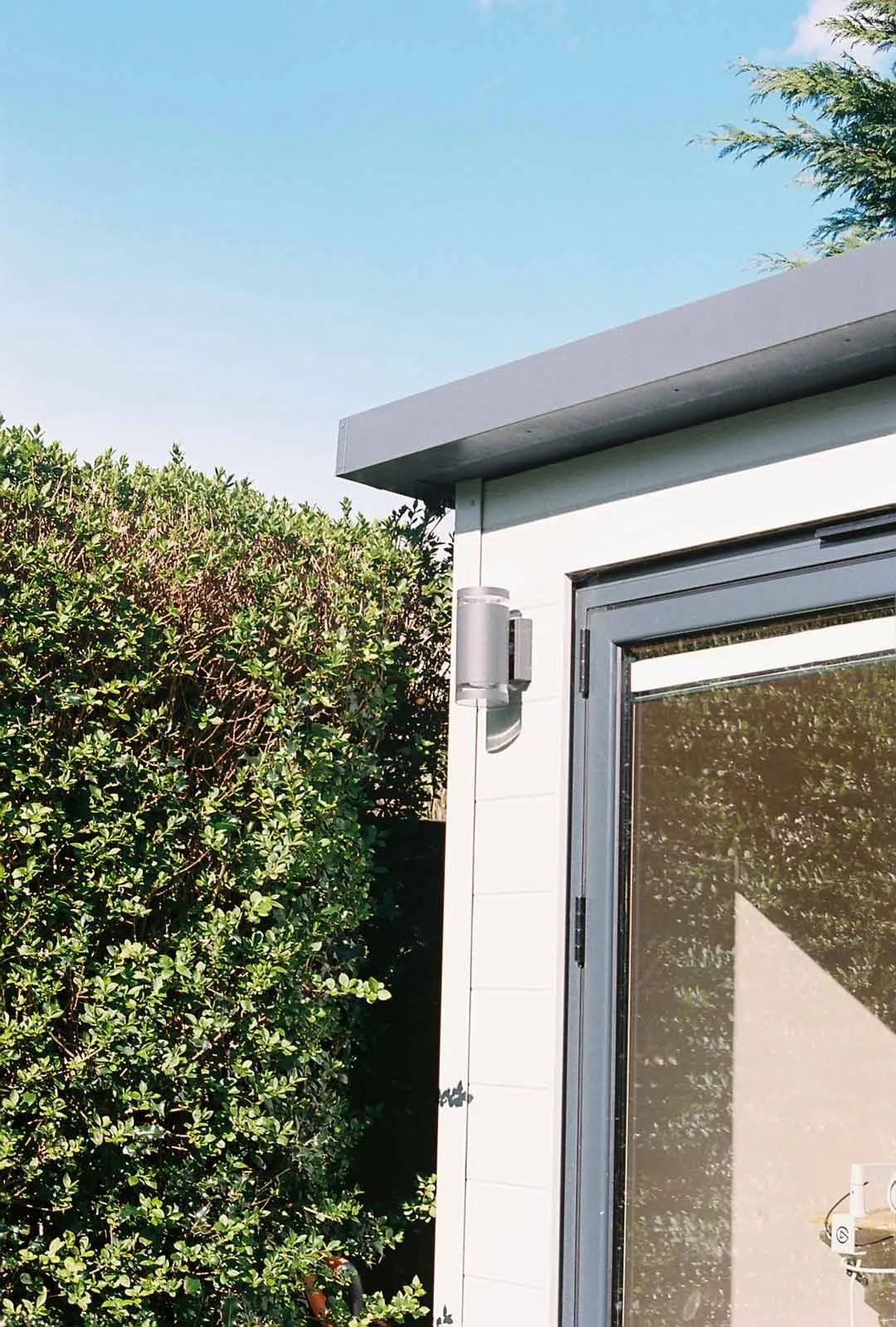 Close-up of bespoke white garden room with composite cladding, aluminium door frame and exterior wall light