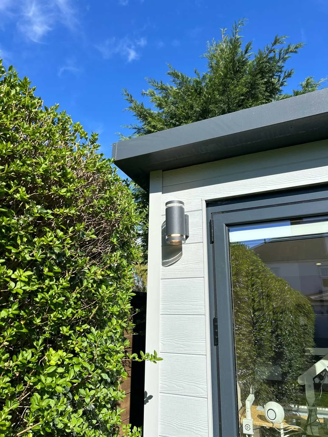 Close-up of bespoke white garden room with composite cladding, aluminium door frame and exterior wall light