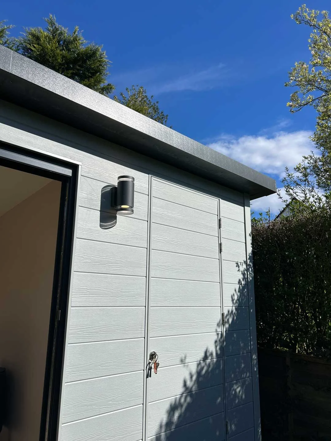 External detail of white garden room with composite cladding and mounted outdoor lighting