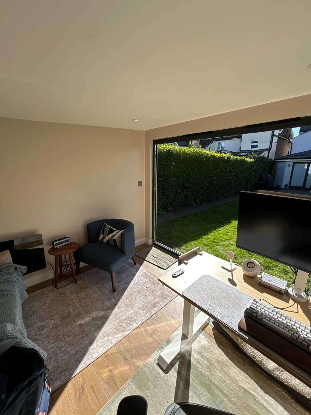 Interior of a bright garden office with desk setup, large window and natural light overlooking the garden