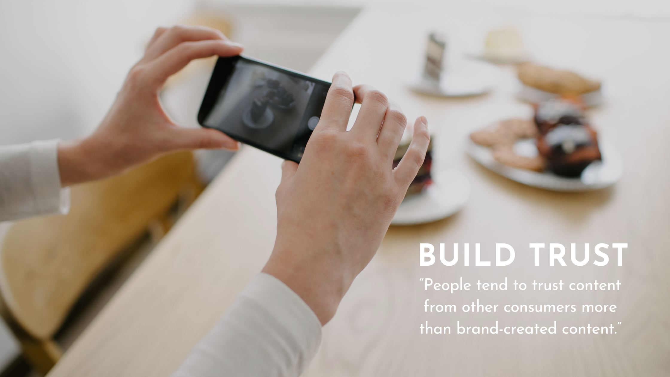 Two hands hold a phone taking a picture of their food on a table in the background with white text in the corner that says "Build trust - people tend to trust content from other consumers more than brand-created content"