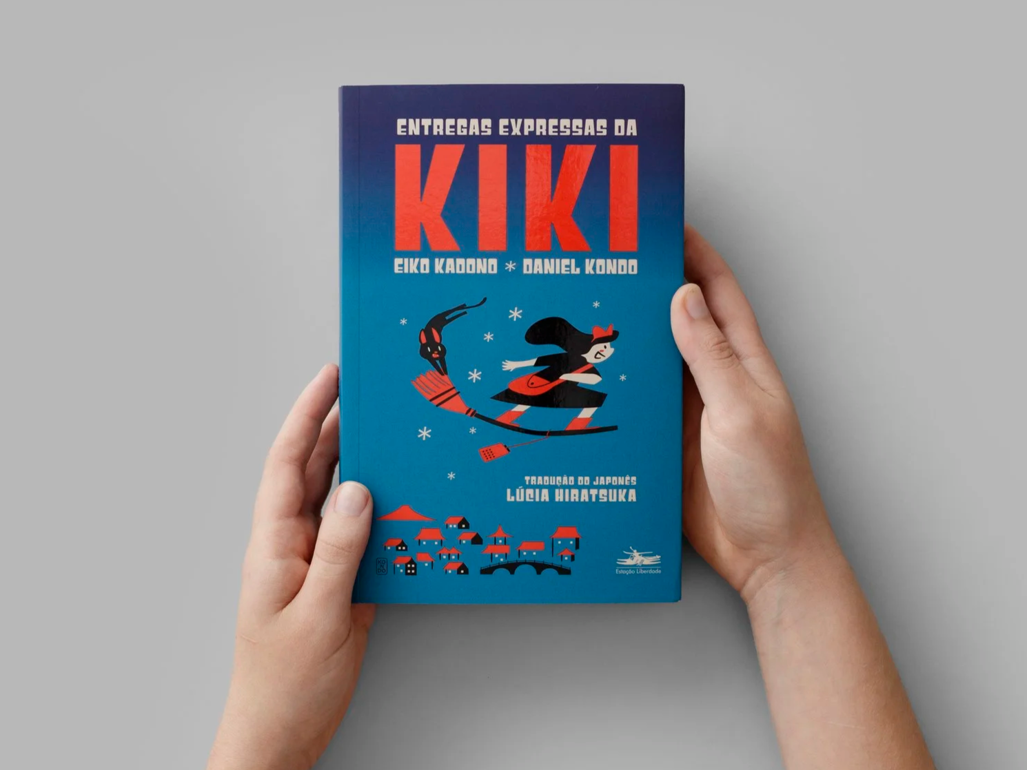 Hands holding the Brazilian edition of Kiki’s Delivery Service by Eiko Kadono, illustrated by Daniel Kondo, showing the blue cover with Kiki flying on a broom.