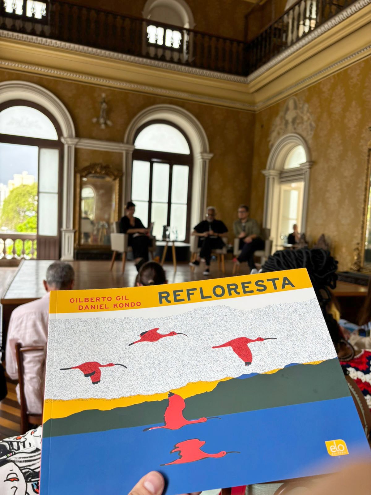 detalhe da capa do livro Refloresta de Gilberto Gil e Daniel Kondo em primeiro plano, e ao fundo eliane Brum, gilberto Gil e Daniel Kondo no palco do Theatro da Paz.