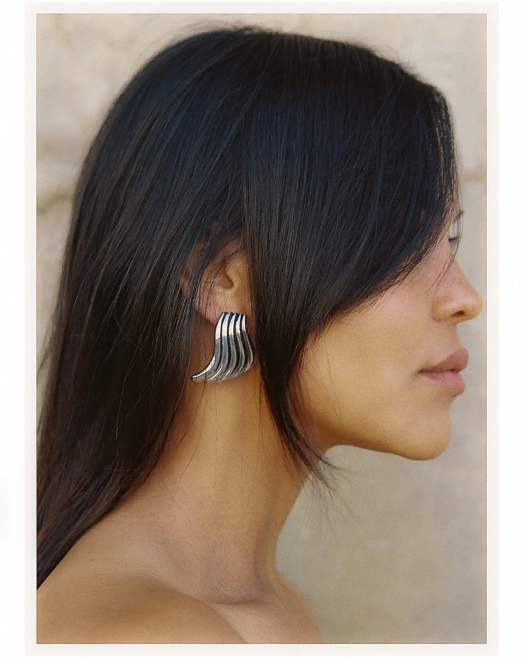 Side profile of a woman with long, straight, dark hair and a silver, wavy-shaped earring.