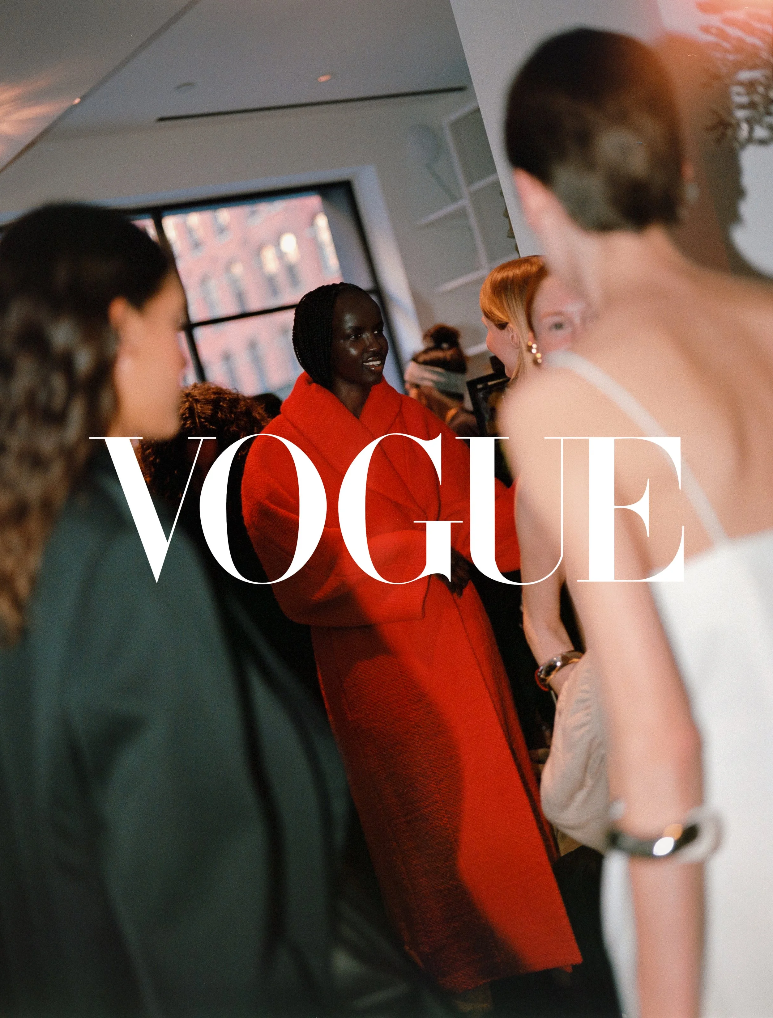 A group of diverse women at a fashionable event, with large windows and city buildings in the background, and the Vogue logo overlayed.