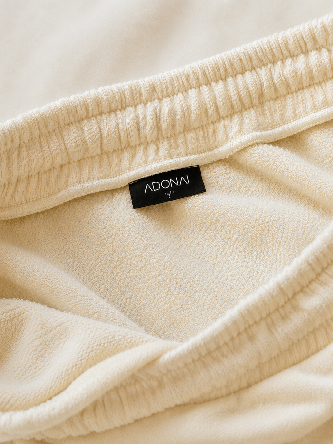 Close-up of a beige Adidas clothing tag inside a beige garment with elastic waistband.