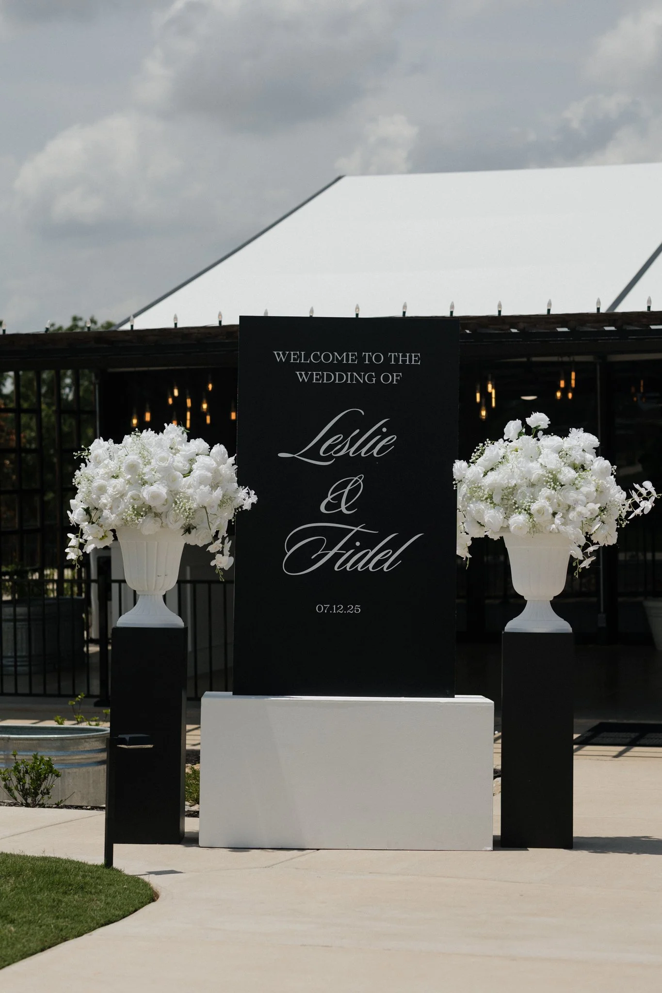 Wedding sign with white floral arrangements welcoming Leslie and Fidel on their wedding day, dated 07.12.25.