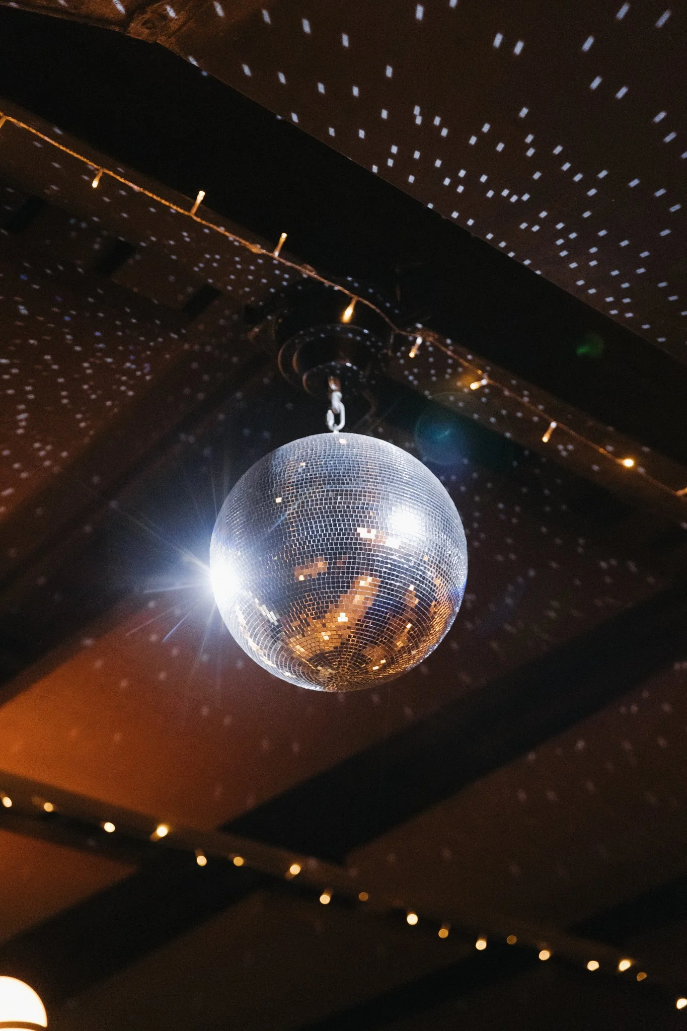 A mirrored disco ball hanging from the ceiling, reflecting light and creating small light spots on the dark ceiling and walls.
