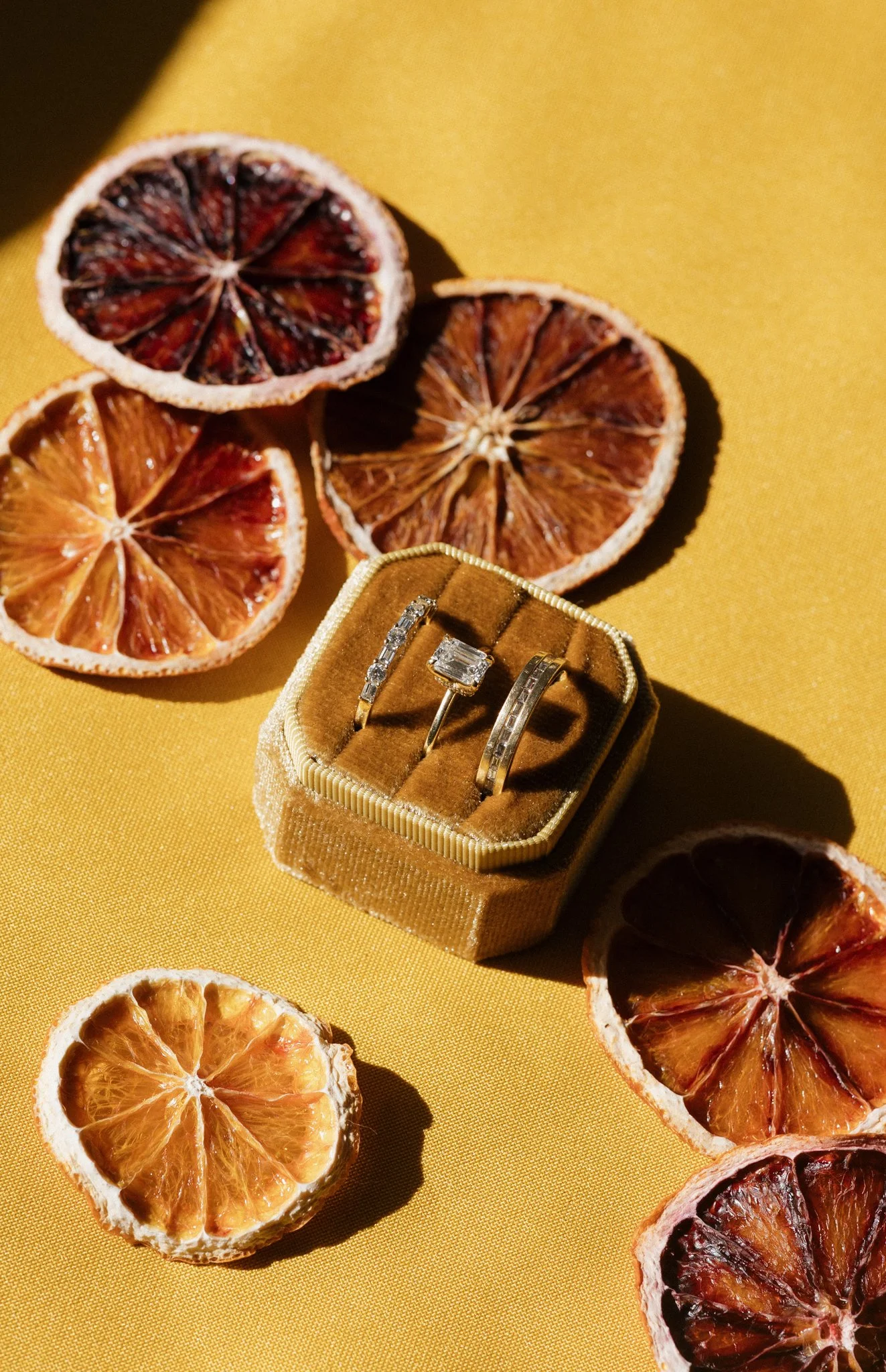 Dried blood oranges and a jewelry box containing three rings on a yellow surface.