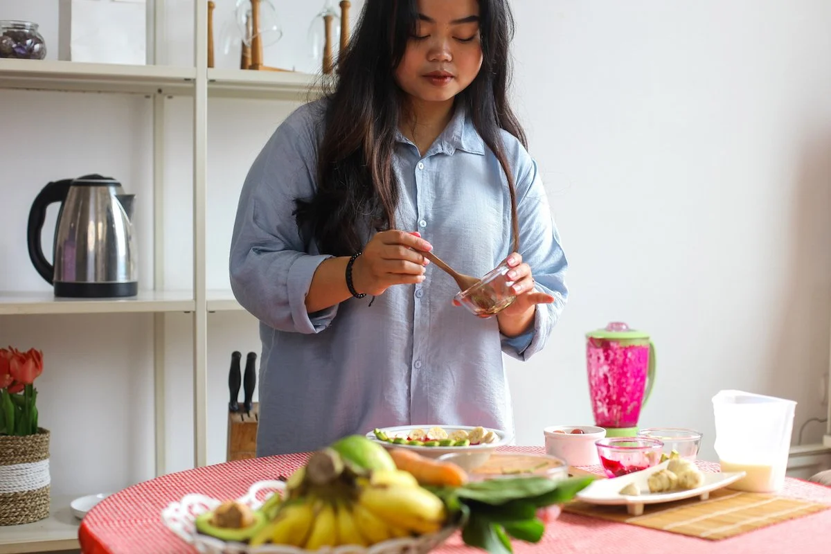woman making smoothie bowl in blue button down shirt
