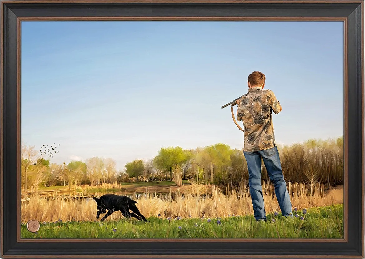 A man with a camo jacket and jeans holding a shotgun stands in a grassy field with a black dog running near him, overlooking a pond and trees under a clear blue sky