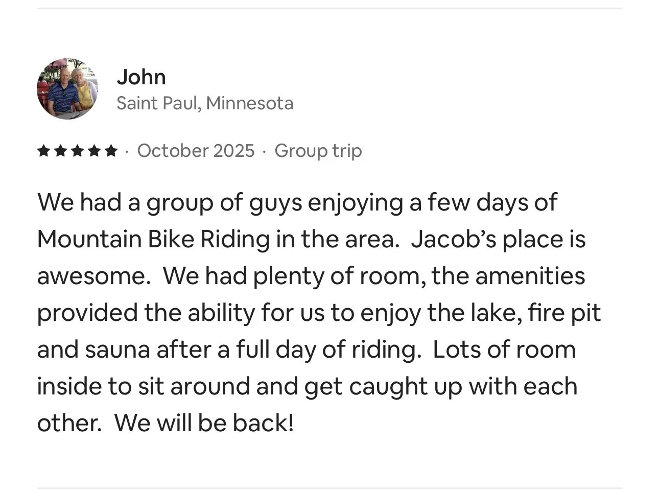 A review on a travel platform from John, who visited Saint Paul, Minnesota, about a group trip in October 2025, describing a mountain bike riding experience, the accommodation at Jacob's place with amenities like lake access, fire pit, sauna, and indoor seating.