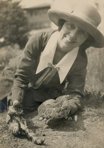 A young woman holding a venomous Gila monster and a rattlesnake in her bare hands.