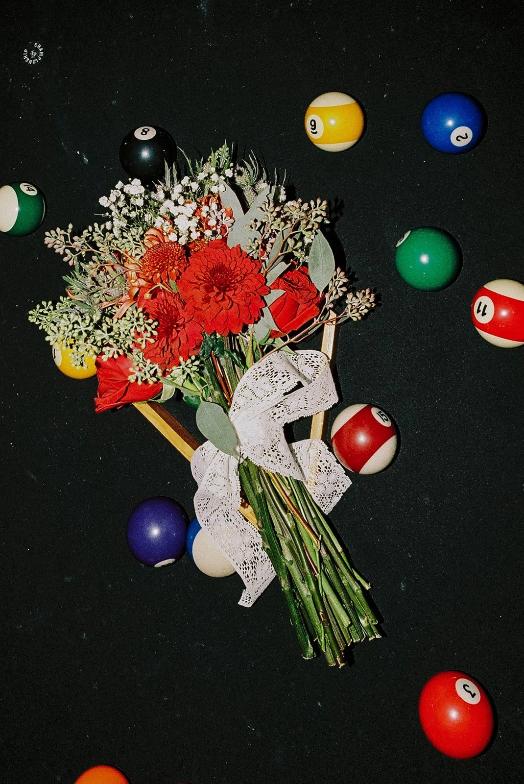 A bouquet of red and white flowers, wrapped with a lace ribbon, placed on a black surface surrounded by colorful billiard balls.