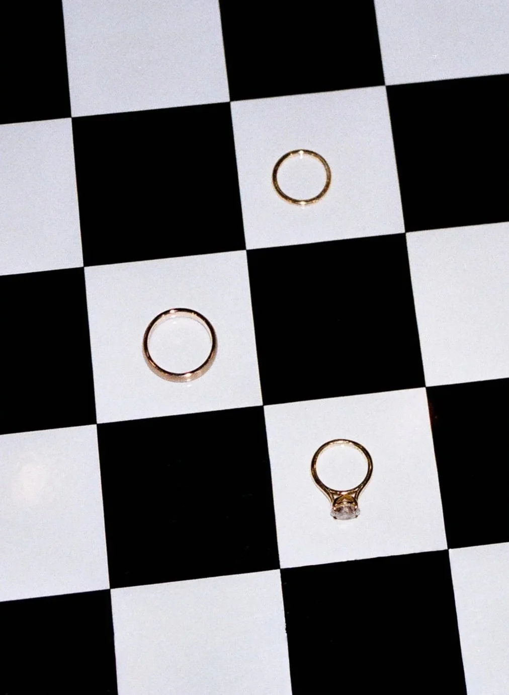 Two plain rings and one ring with a gemstone on a black and white checkered surface.