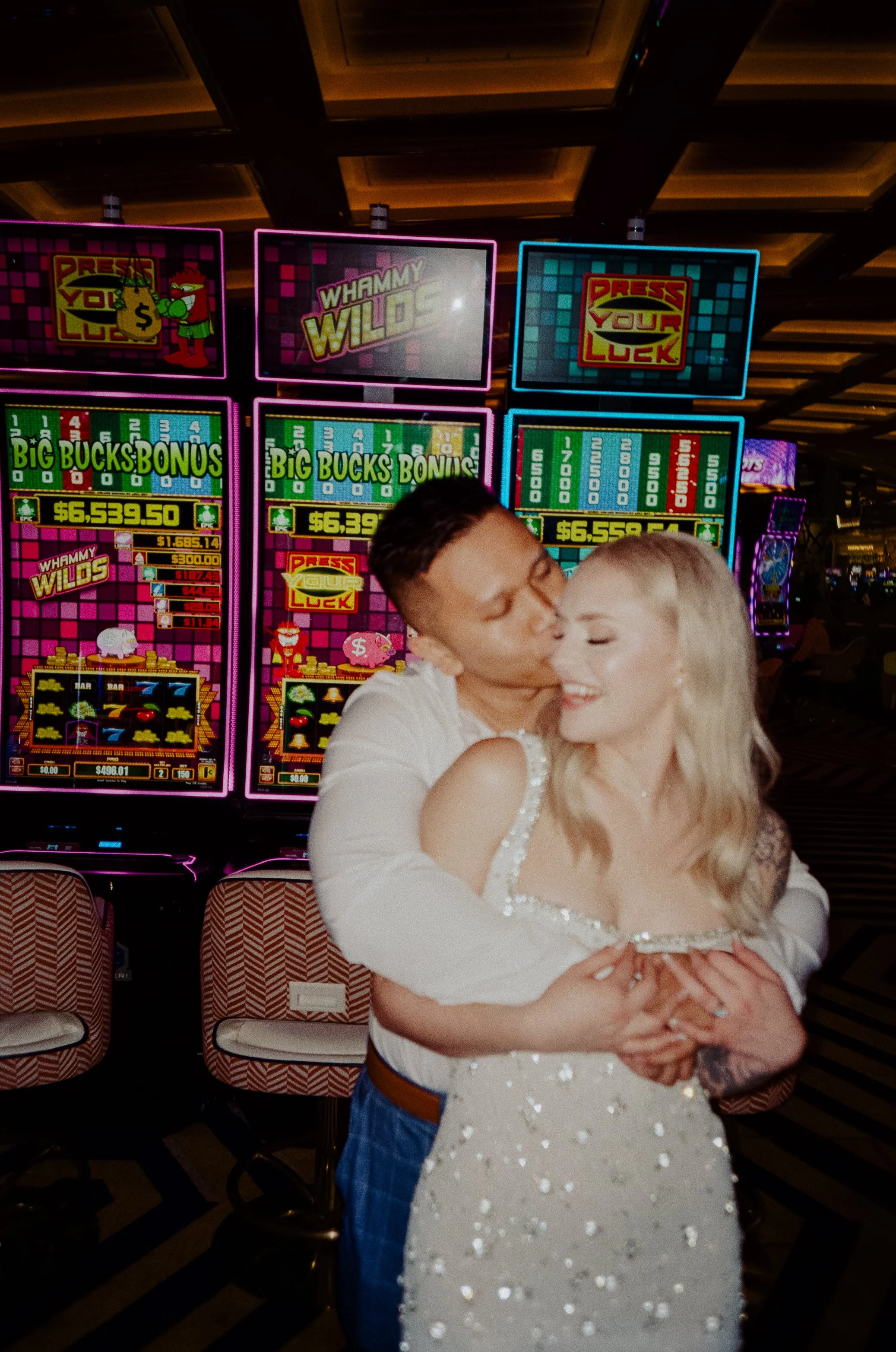 A couple embraces and kisses in front of slot machines at a casino.