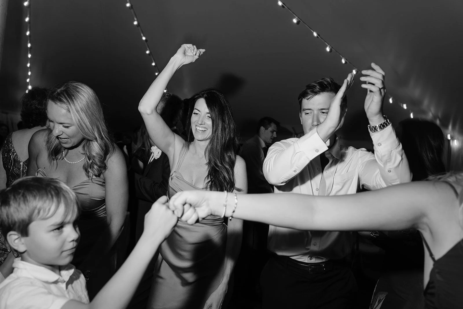 People dancing and having fun at a party or celebration in a decorated venue with string lights.