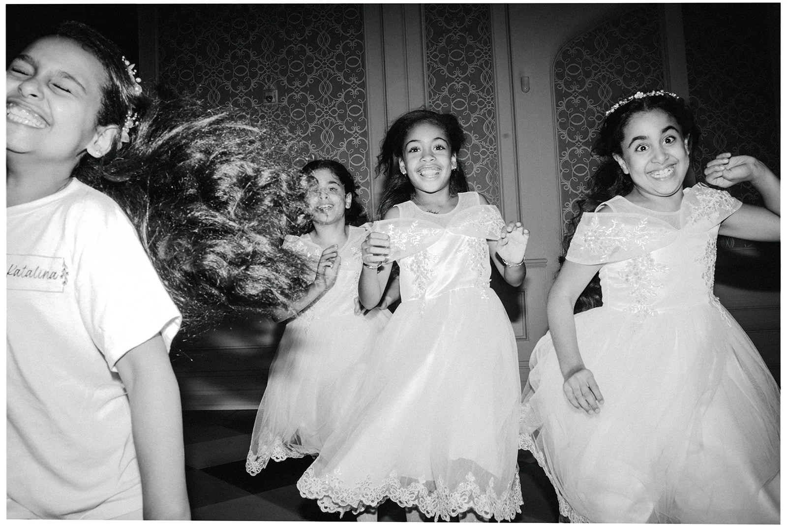 Group of young girls in elegant dresses laughing and dancing at party.
