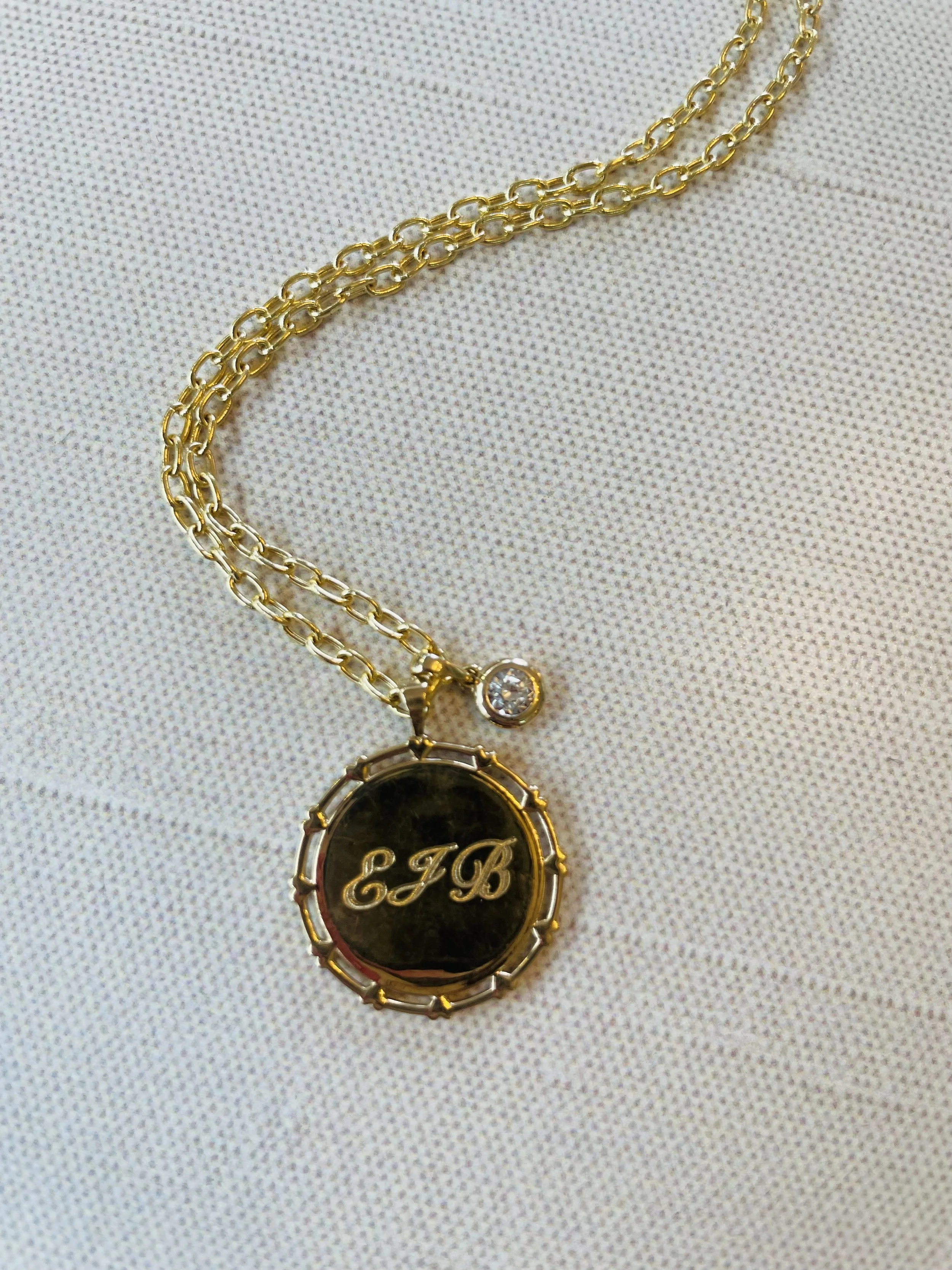 Gold chain necklace with an oval pendant engraved with the initials 'EGB' and a small attached gemstone.