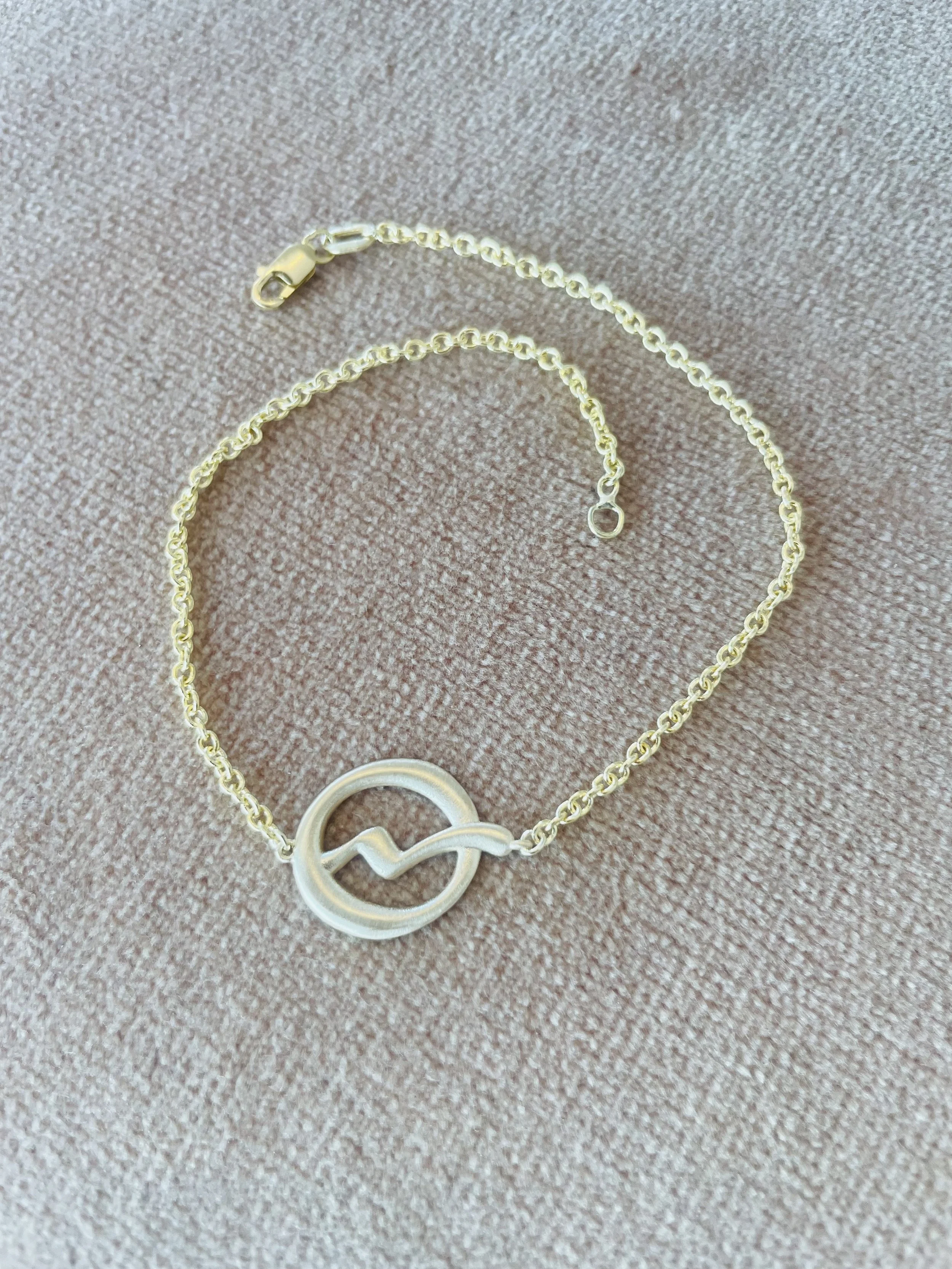 Gold necklace with a round pendant featuring a zigzag design on a pink fabric background.