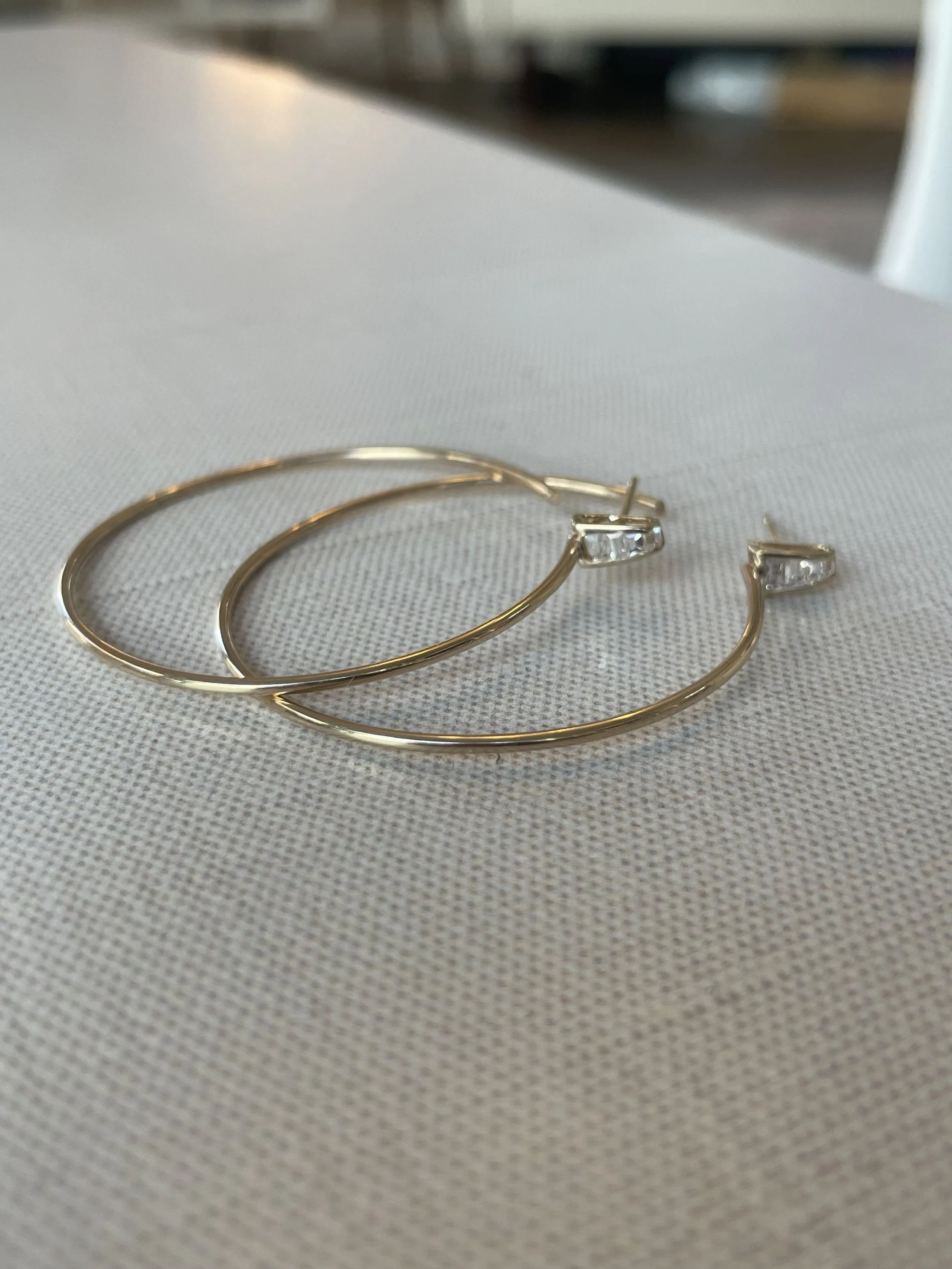 Gold hoop earrings with small rectangular gemstones on a textured fabric surface.