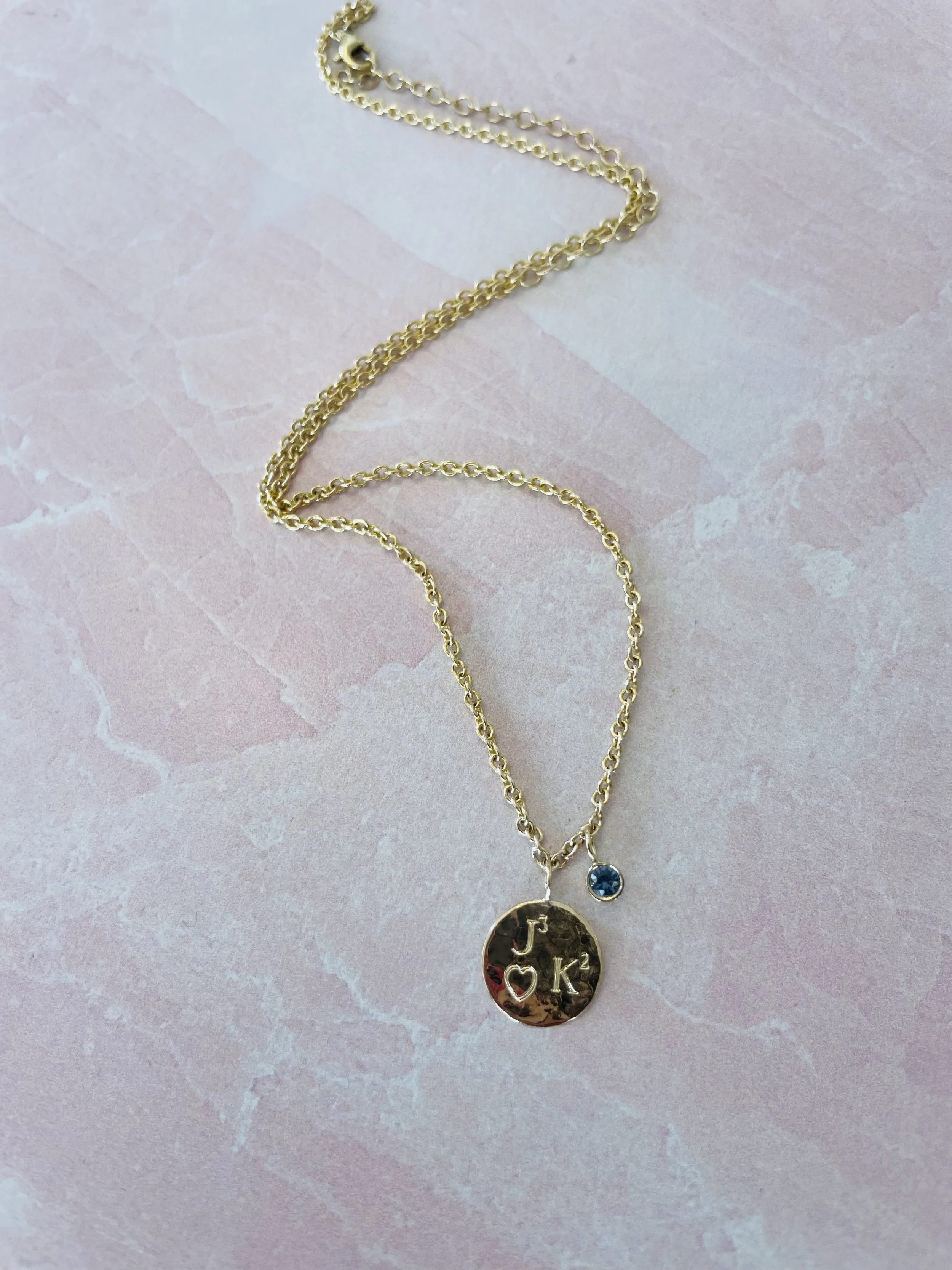 Gold necklace with two pendants on a pink marble background.