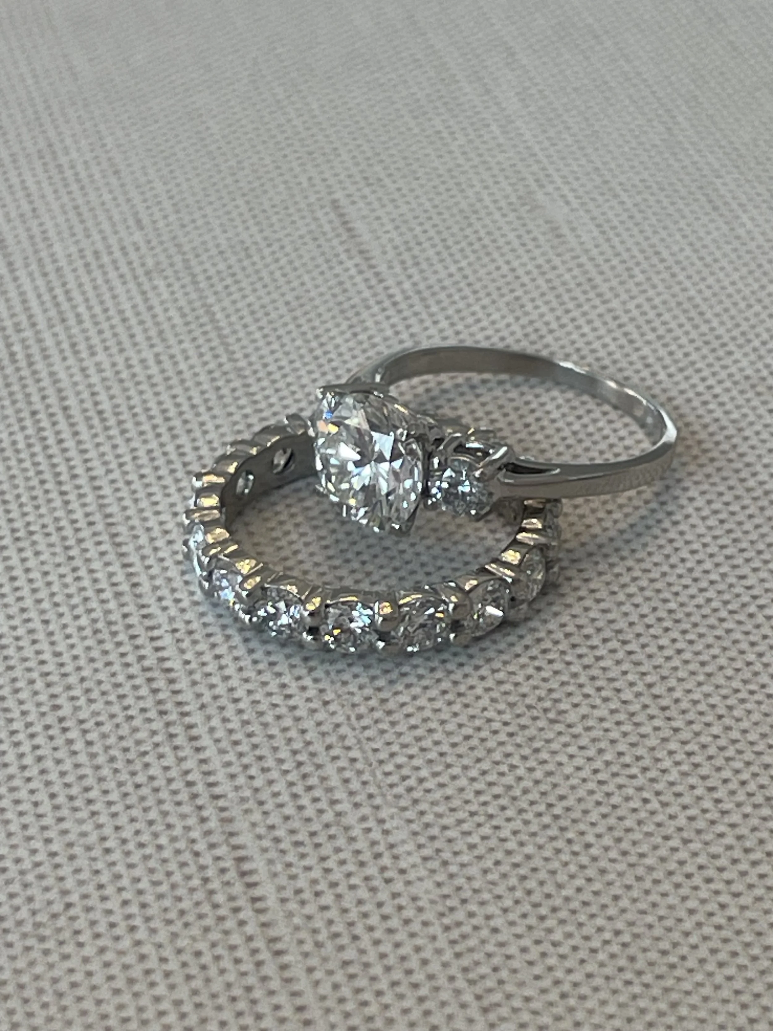 Two silver rings with diamonds placed on a textured fabric surface, one with a large central diamond and the other a halo style with multiple smaller diamonds.