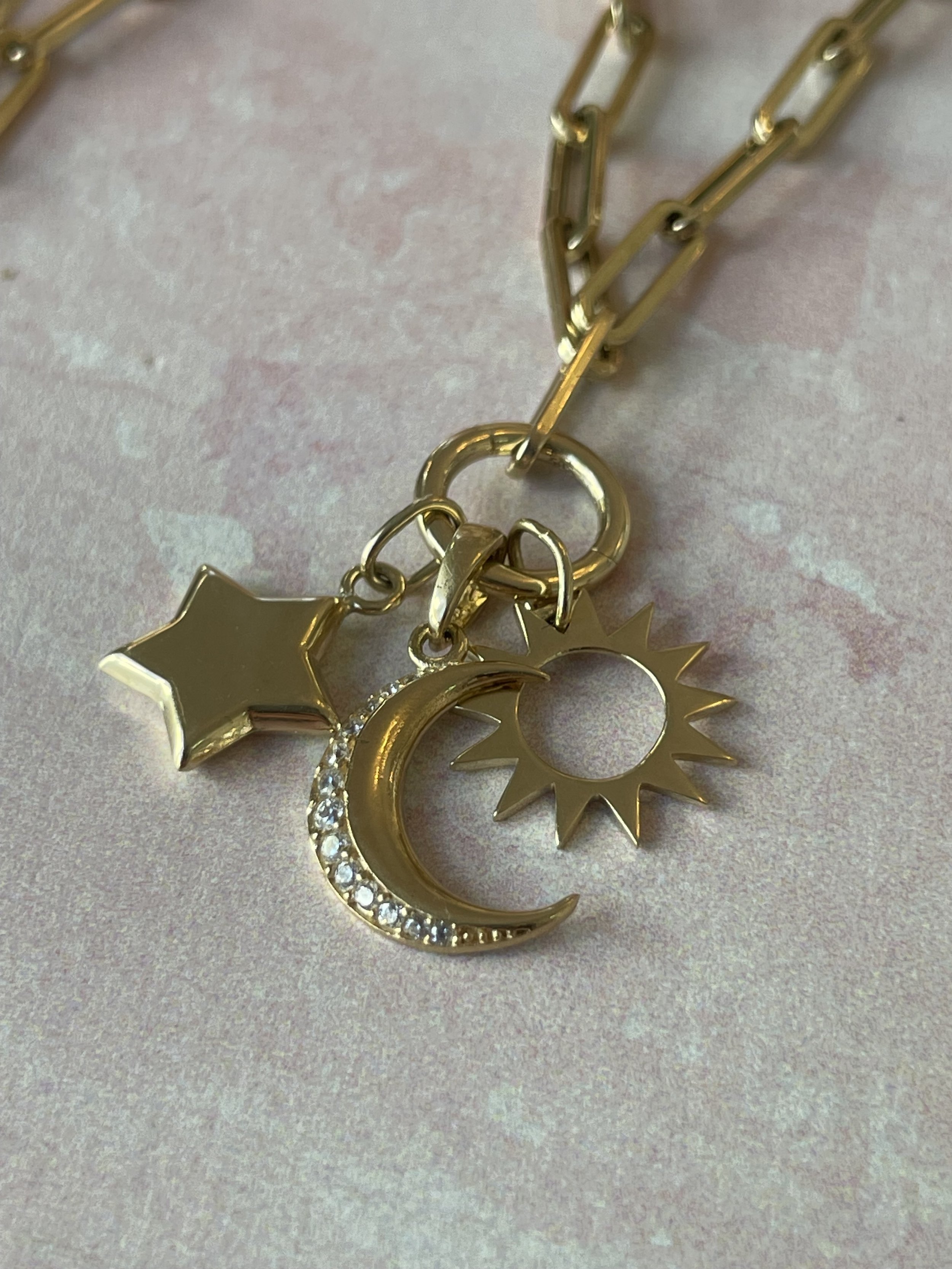 Golden necklace with three charms: star, crescent moon embedded with rhinestones, and sun.