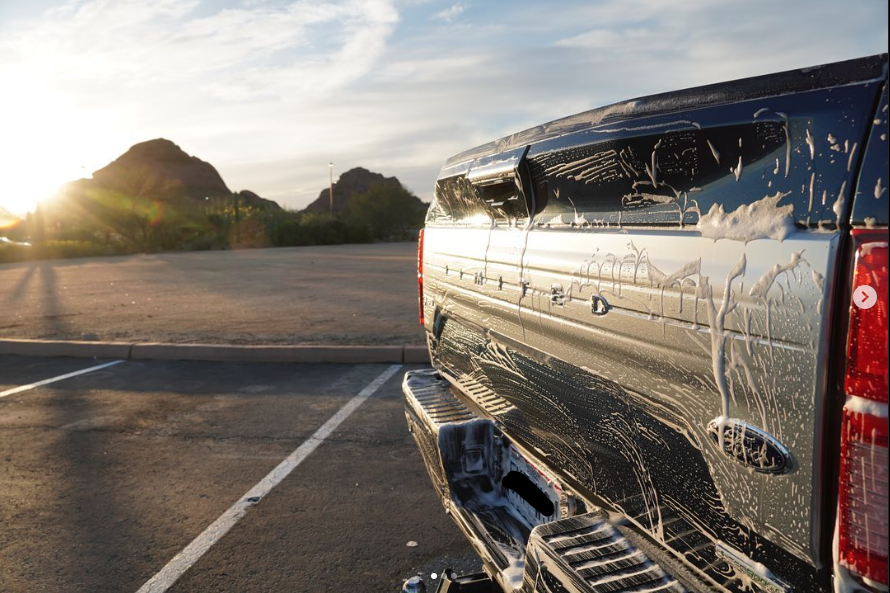 A black pickup truck with soap suds on its back in an empty parking lot during sunset, with mountains in the background.