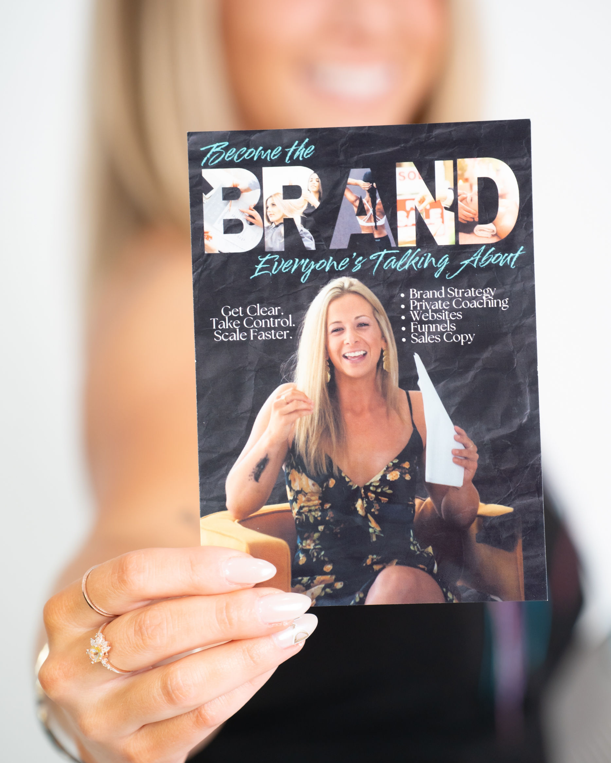 A woman holding a promotional flyer for a branding and coaching business, smiling, with focus on the flyer.