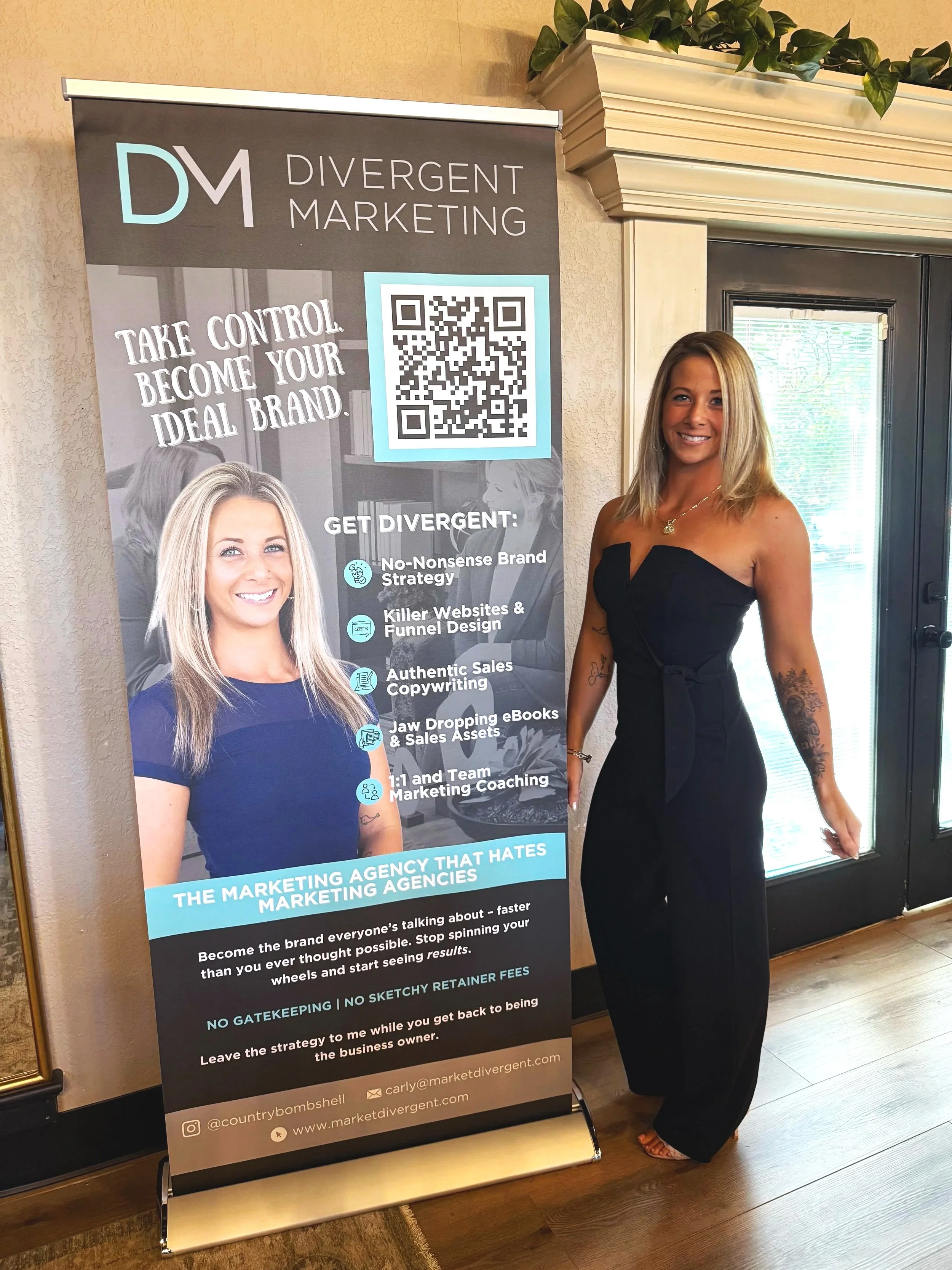 A woman in a black strapless jumpsuit standing next to a promotional banner for Divergent Marketing, featuring a smiling woman in a blue shirt, QR code, and marketing services listed.