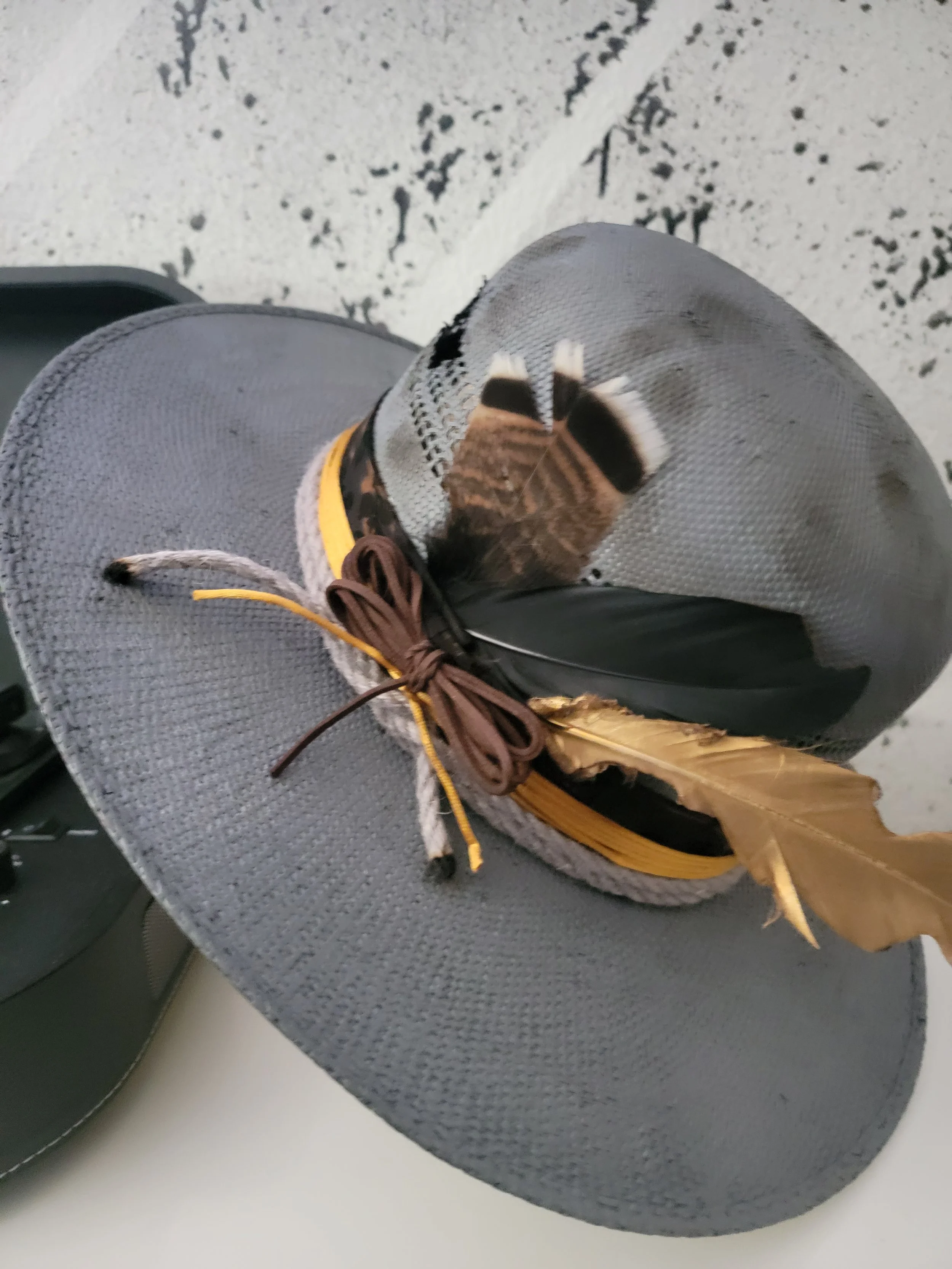 A gray wide-brimmed open crown straw hat with the finishes of a variation wild cought feathers, lace ribbon, and a touch of distress.