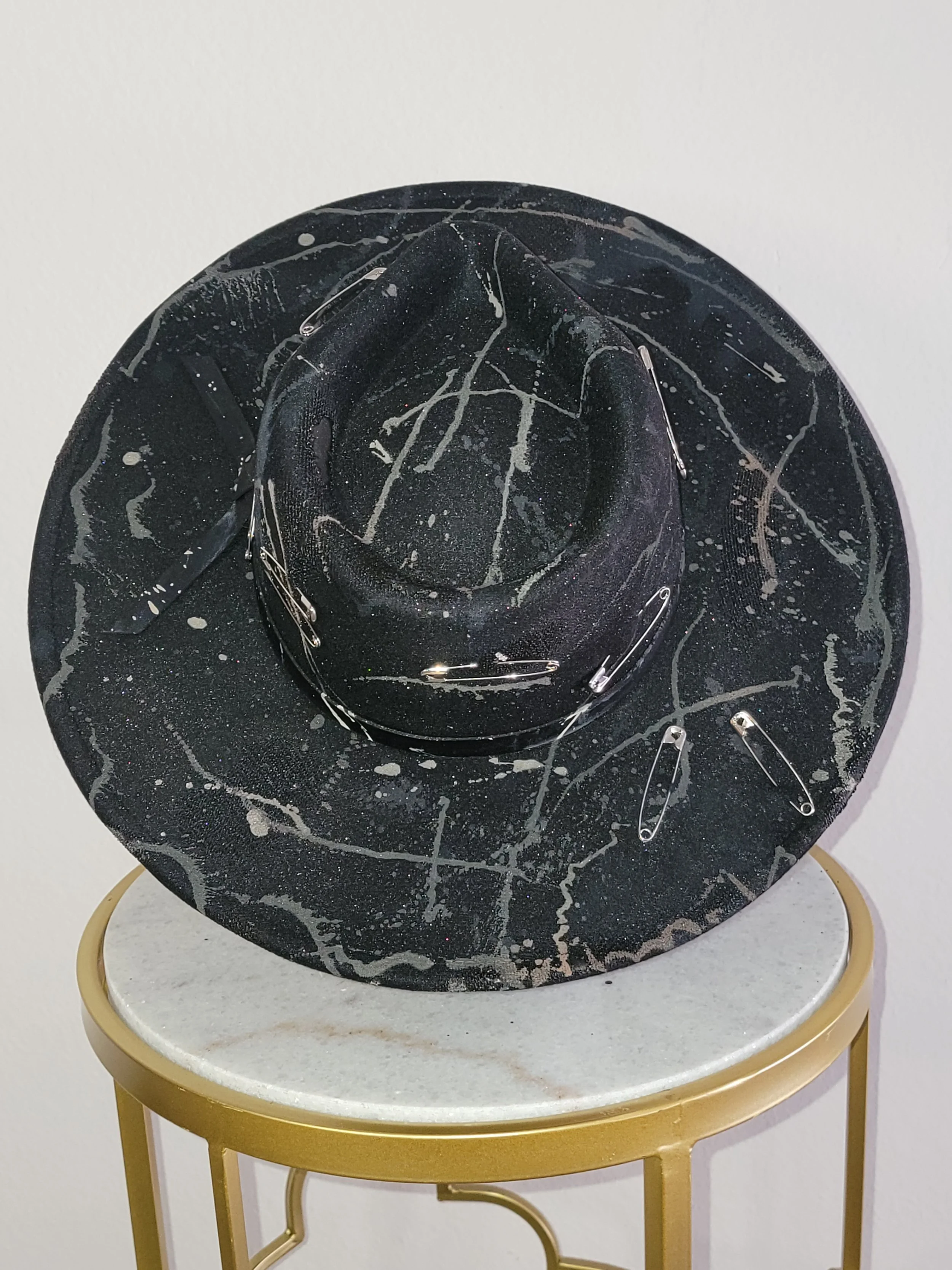 Black teardrop rancher hat with white splattered paint streaks, embellished with safety pins and a black leather band.