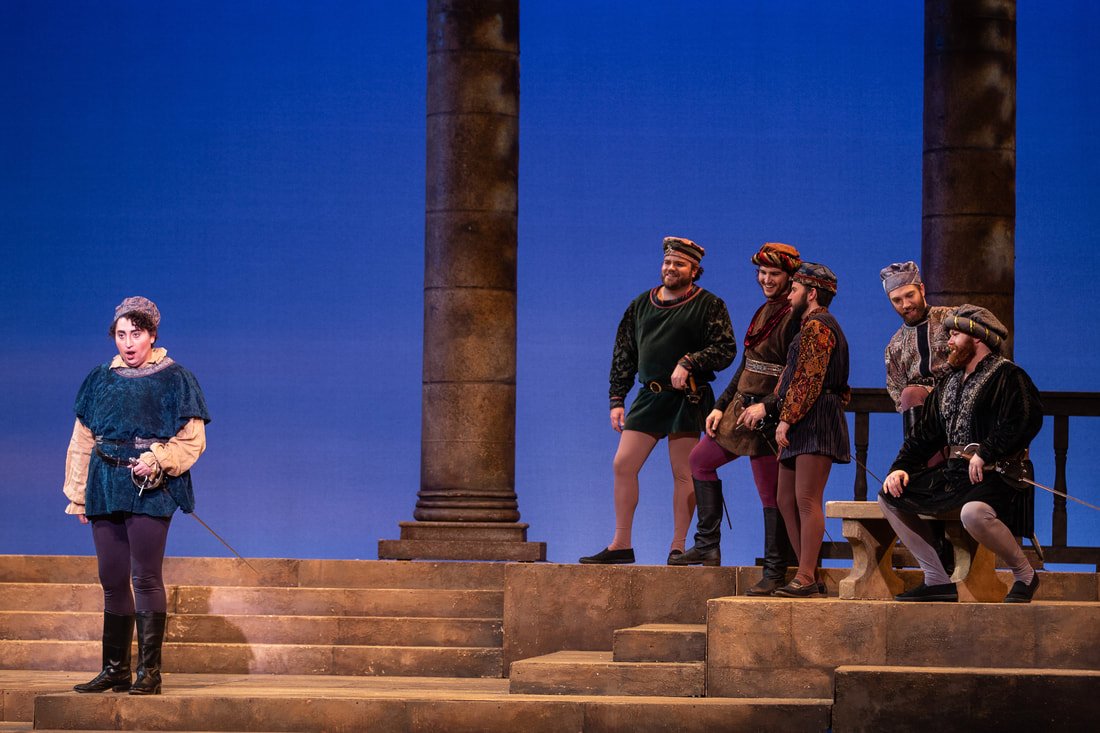 Theatrical performance with actors in Renaissance costumes on stage with columns and steps.