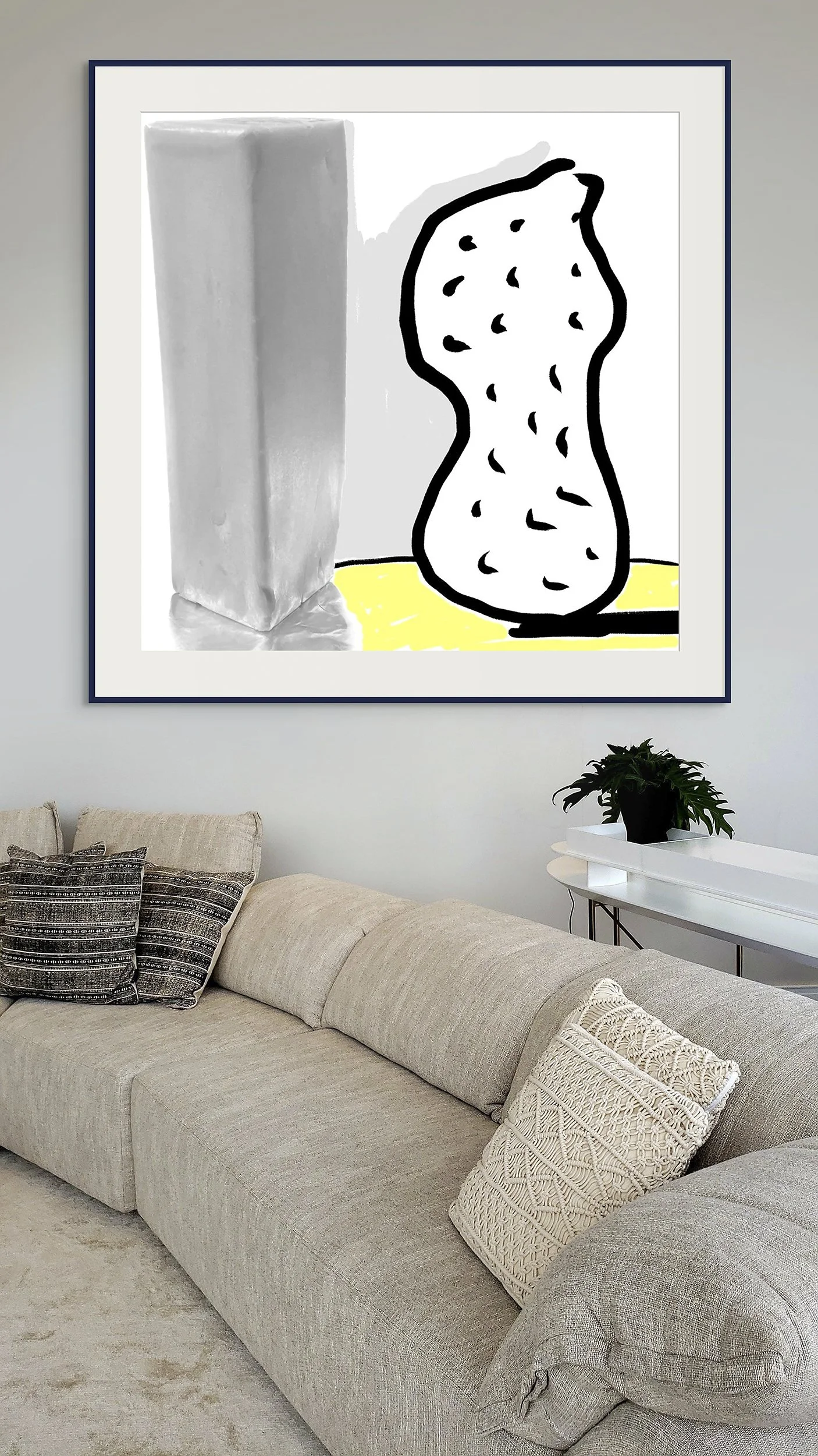 Mock-up showing matted and framed print of Surrealistdigital composite, Peanut | Butter, on gray wall, behind couch that curves toward viewer with warm/neutral-colored upholstry and pillows.