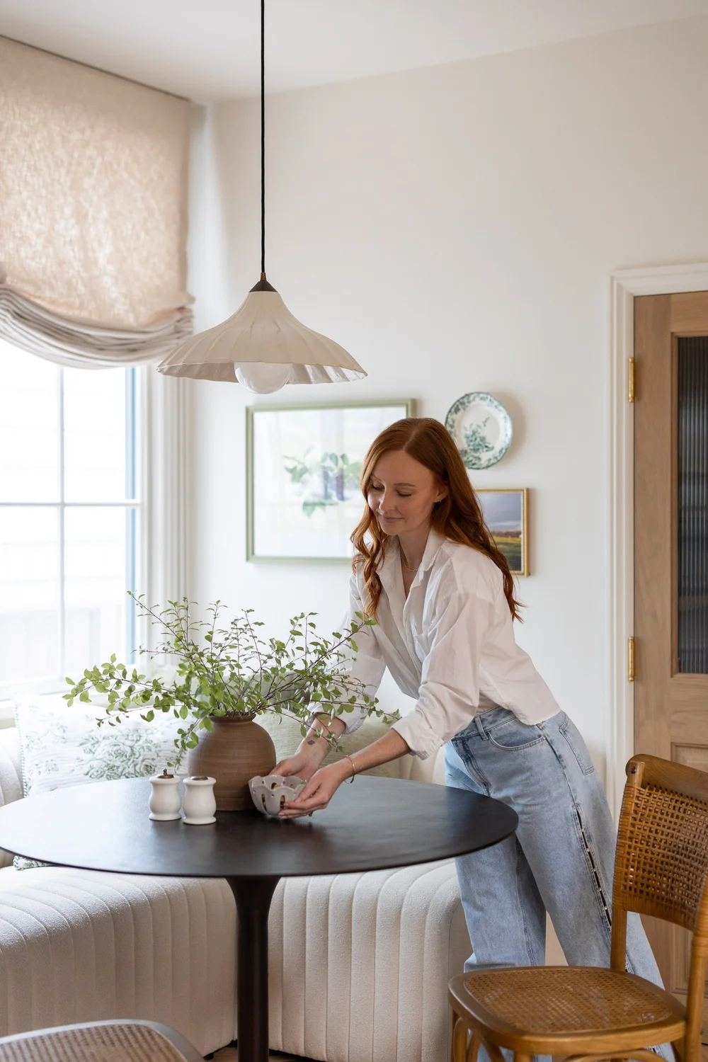 Kelli Daley arranging a plant on a round dining table in a banquette nook