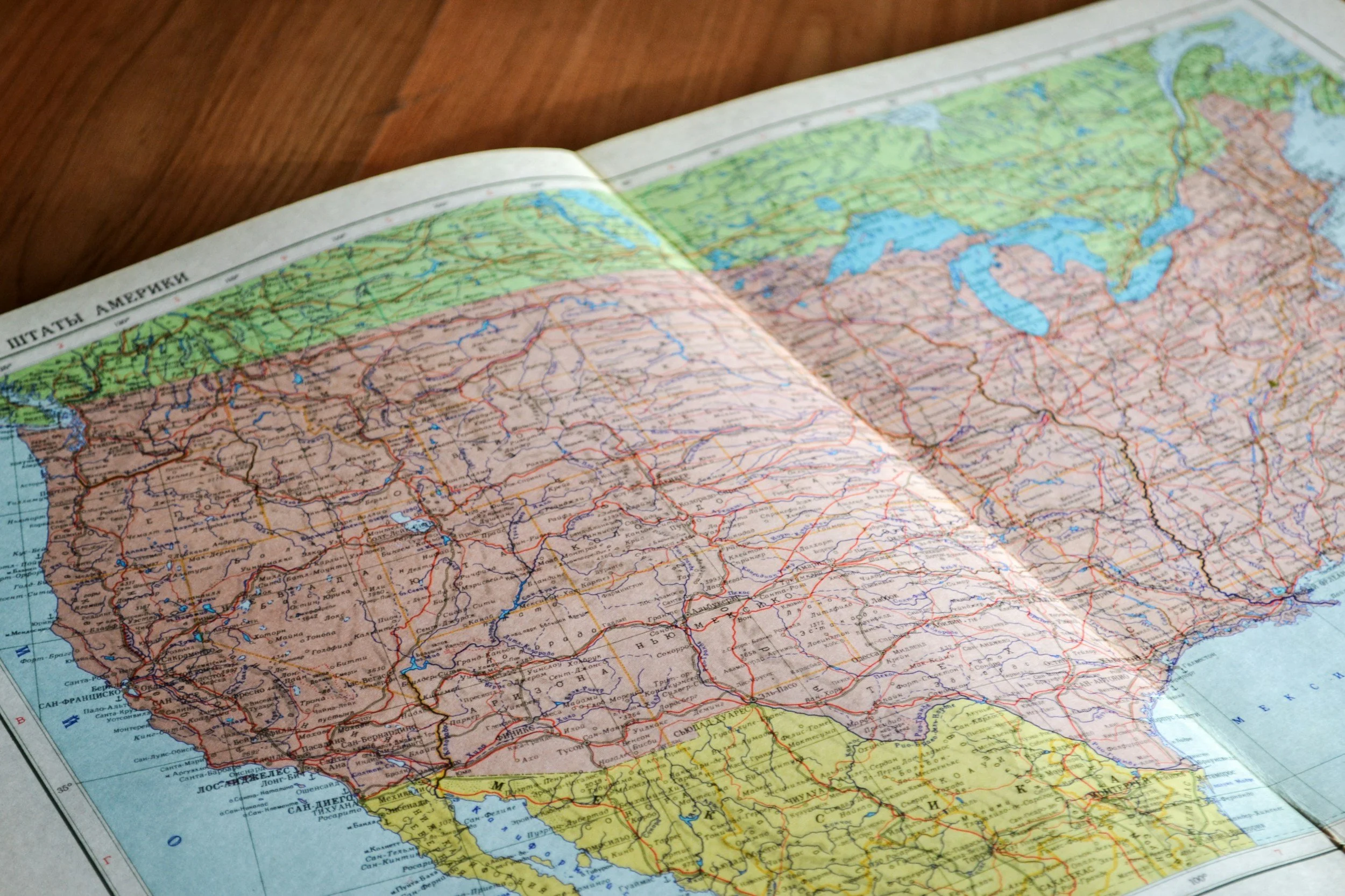 A detailed map of the United States of America, showing states, highways, and geographic features. The map is open on a wooden surface.