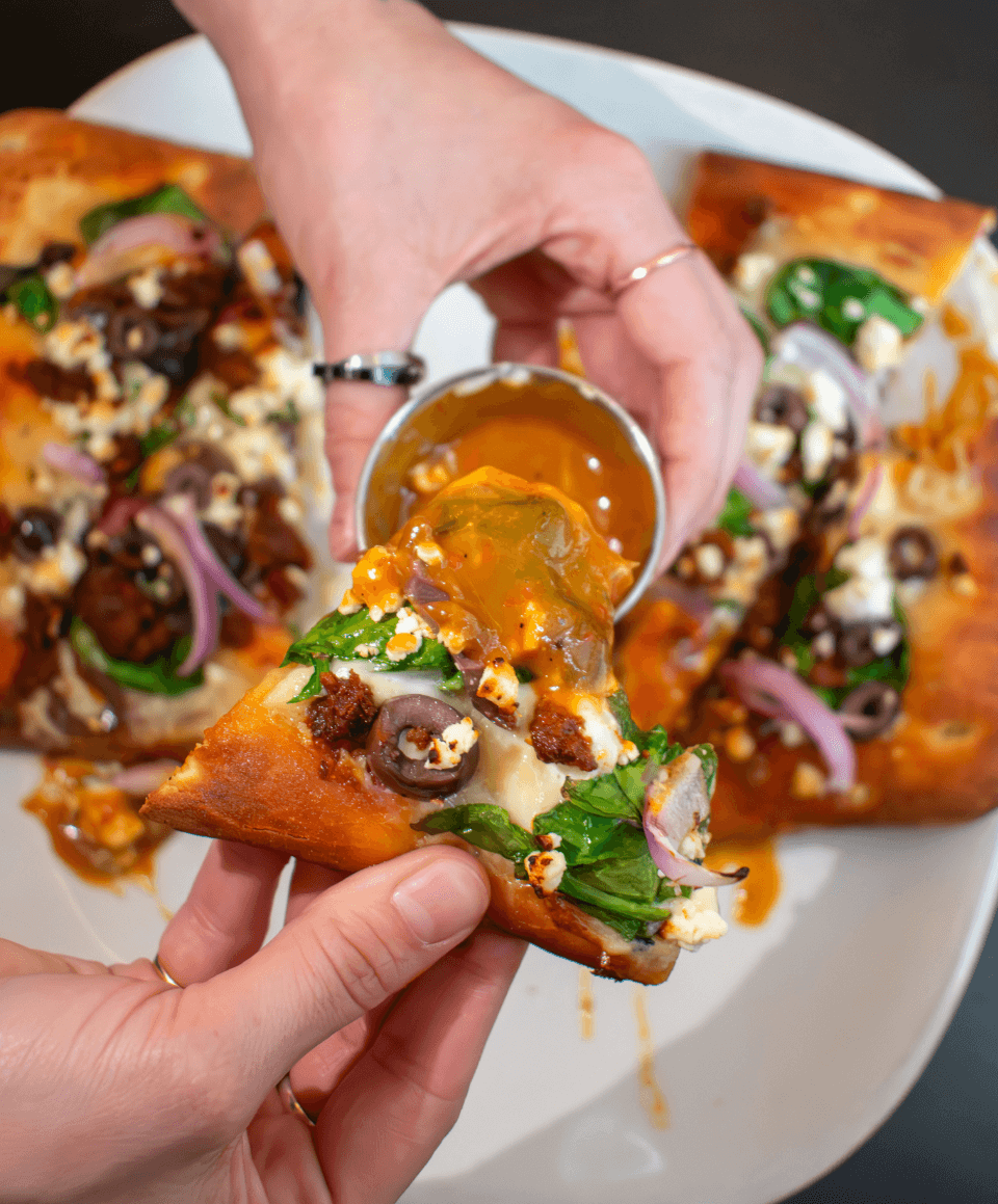 hand-with-rings-dipping-flatbread-pizza-into-orange-red-sauce-eat-drink-crave-2024.png