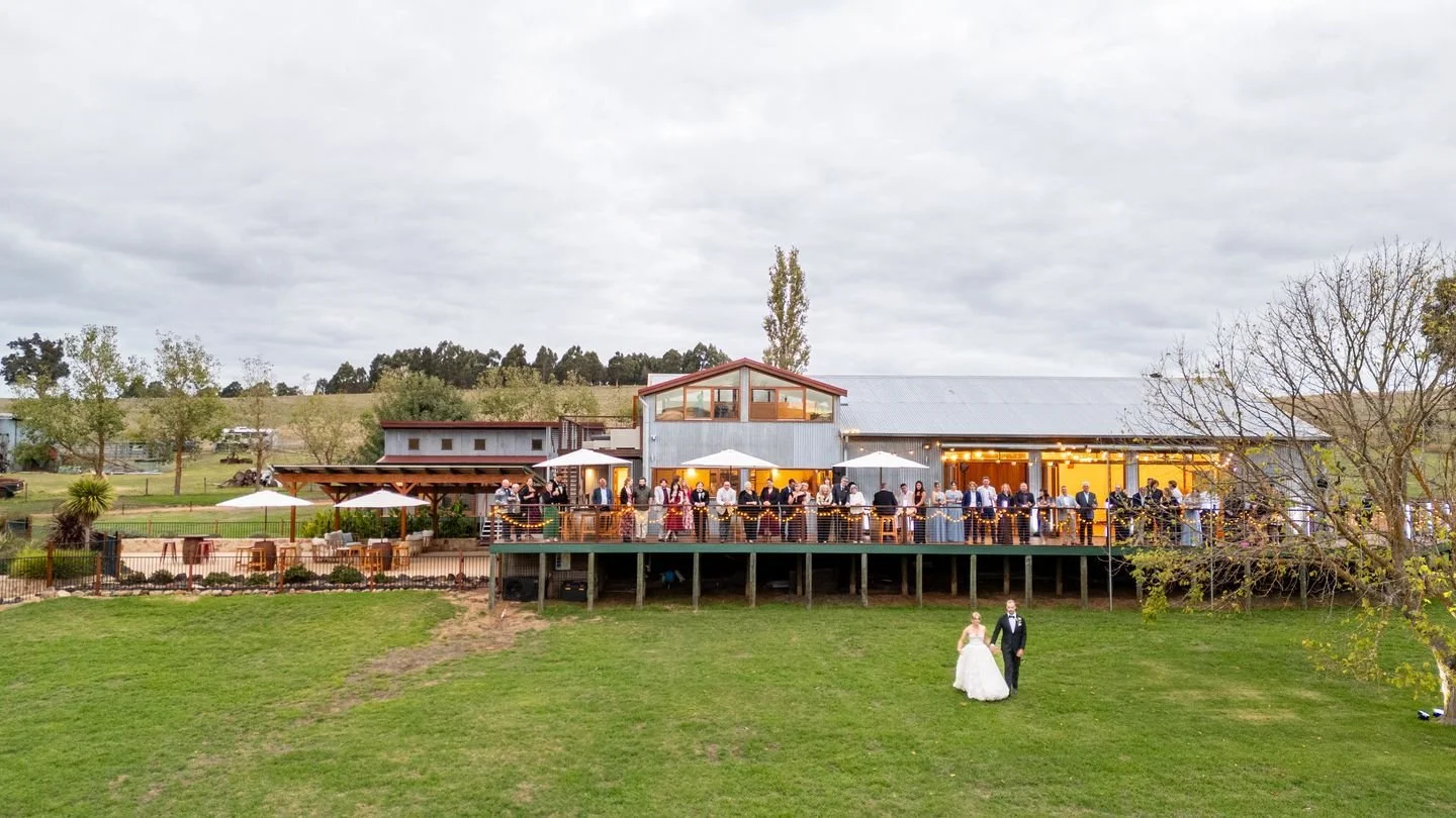 The late afternoon light stretching across the valley, catching the string lights on the deck. From above, you can see the shape of a celebration unfolding. The quiet hum of conversation drifting from the shearing shed. A slow walk across the lawn. T