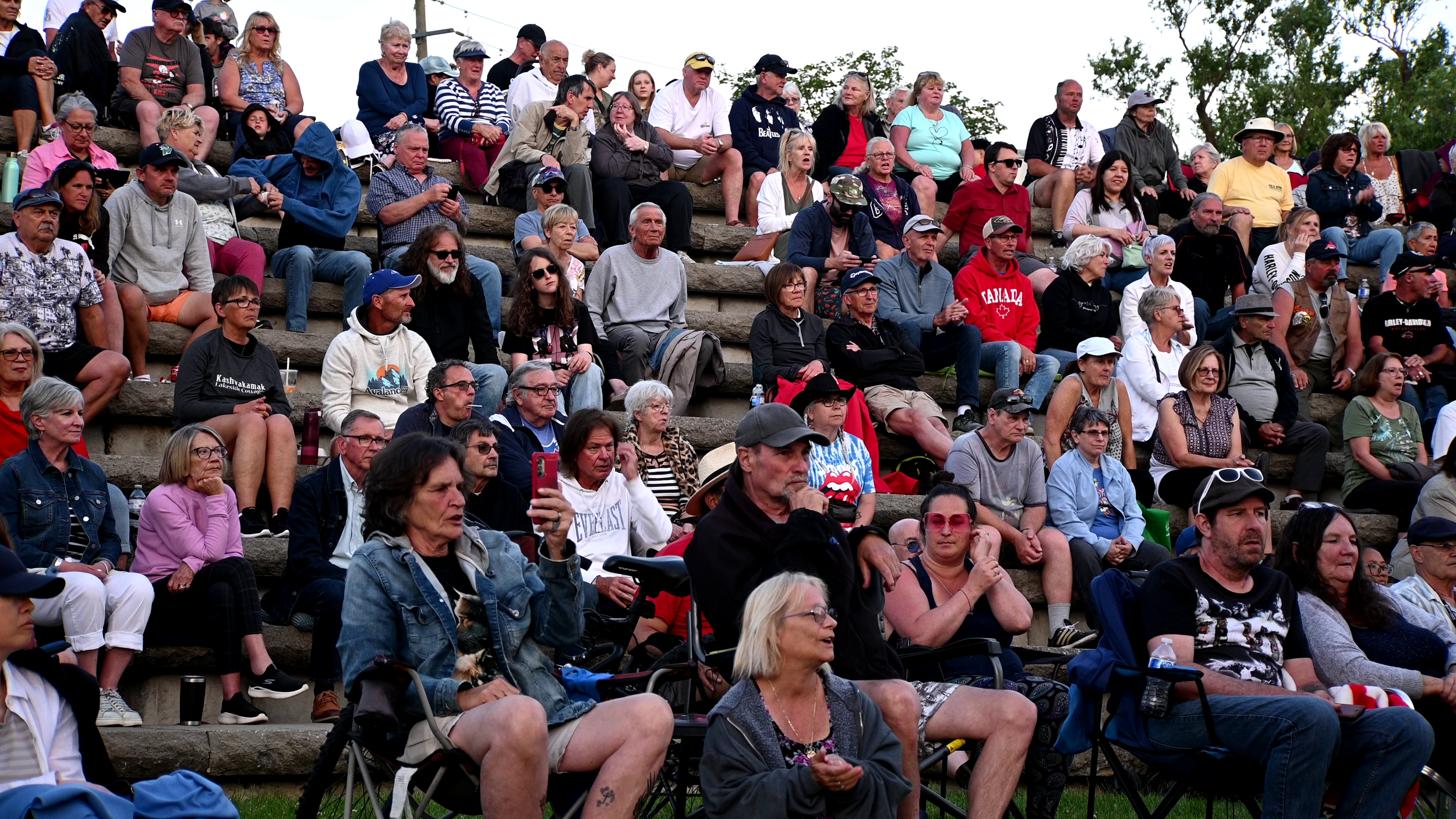A large crowd of people sitting on stadium steps outdoors, attending an event during daytime.