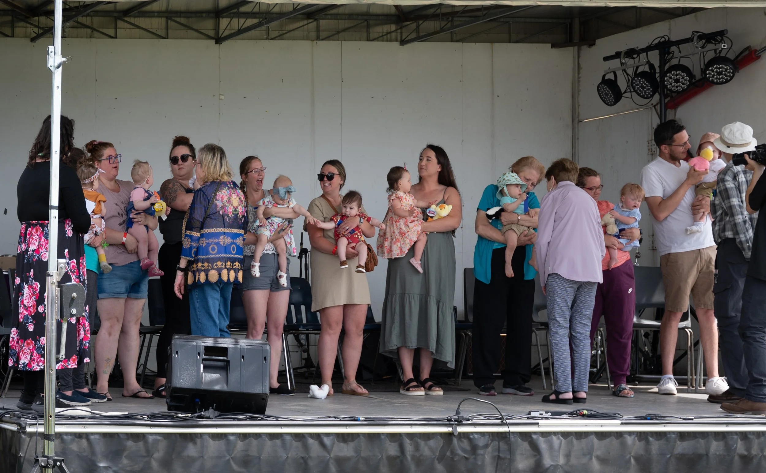 Group of adults and children on stage during a puppet show, some children holding puppets, with a man playing with a puppet on the right.