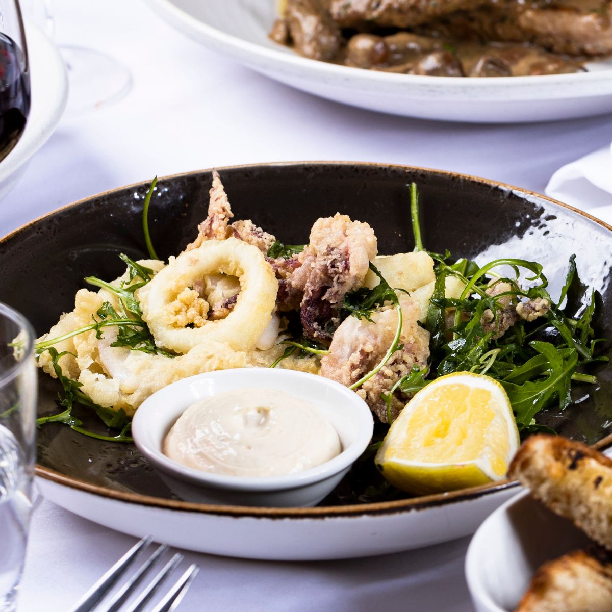 Fried calamari with lemon wedge, parsley, and dipping sauce on a black plate