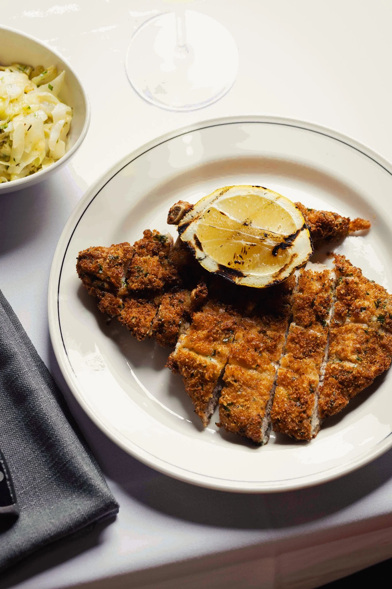 A plate of breaded and sliced meat topped with a grilled lemon wedge, served with a side of coleslaw and a napkin.