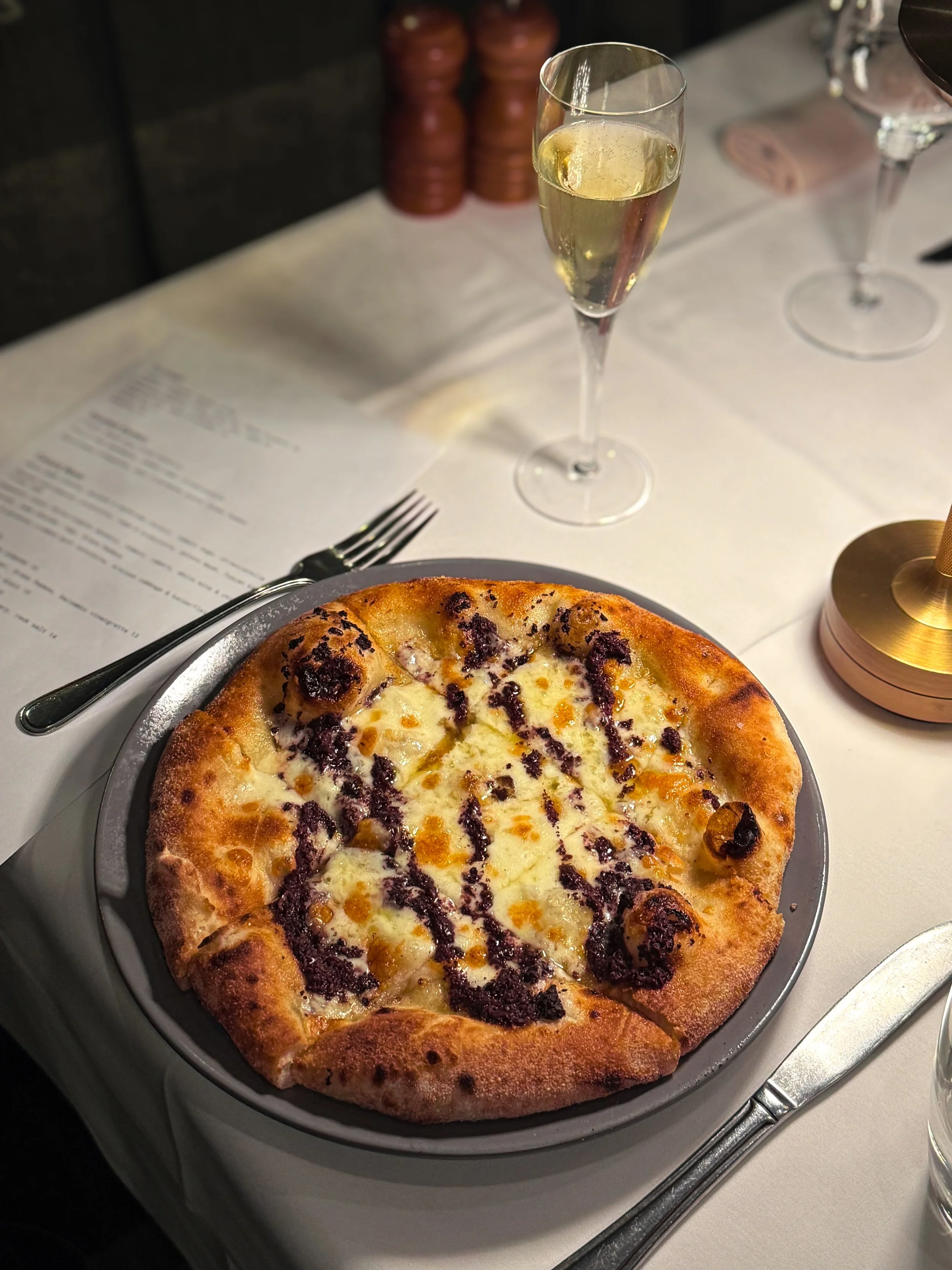 Pizza with cheese and dark sauce on a place setting with a glass of white wine and a menu nearby.