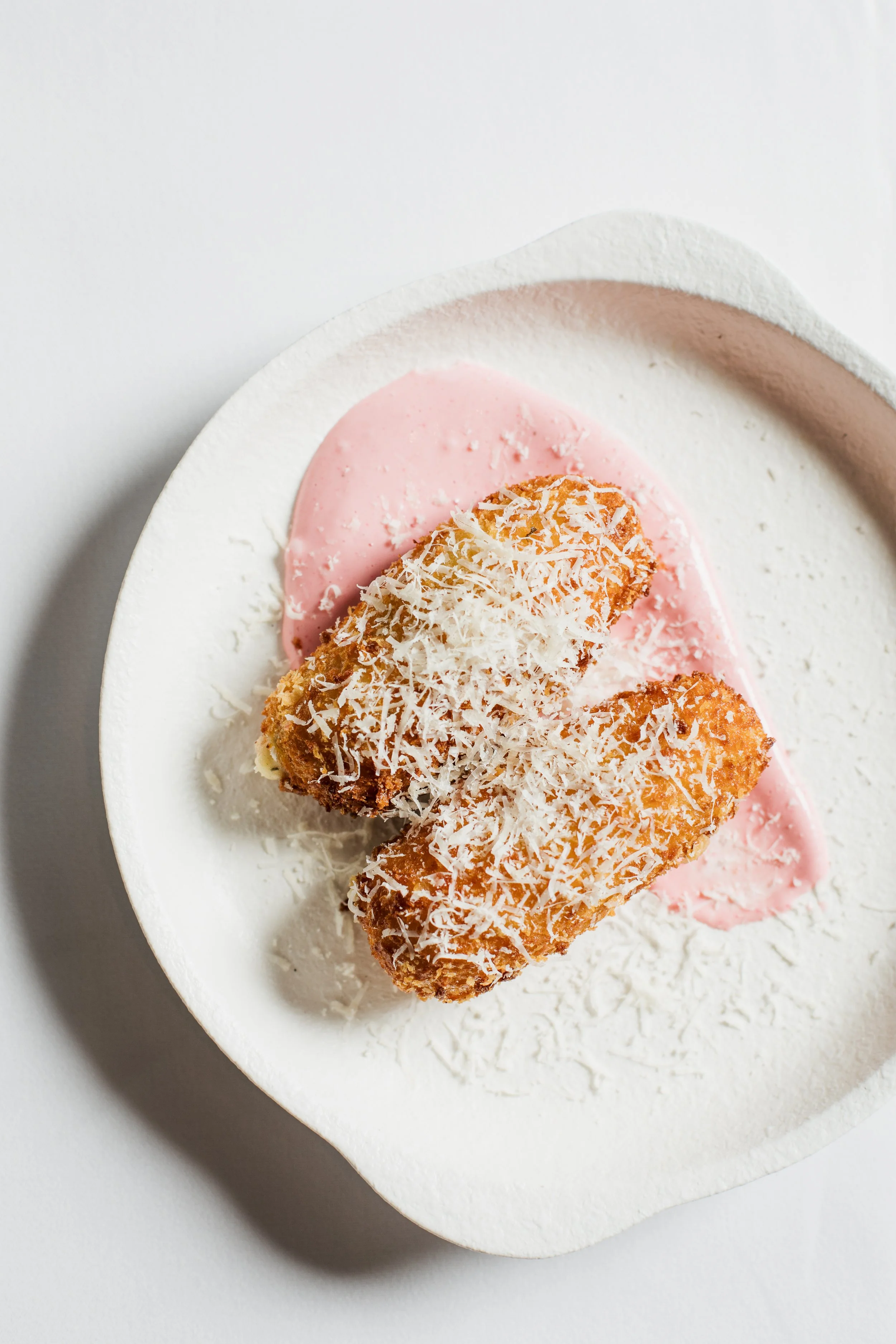Breaded and fried food with white cheese and pink sauce on a white plate.
