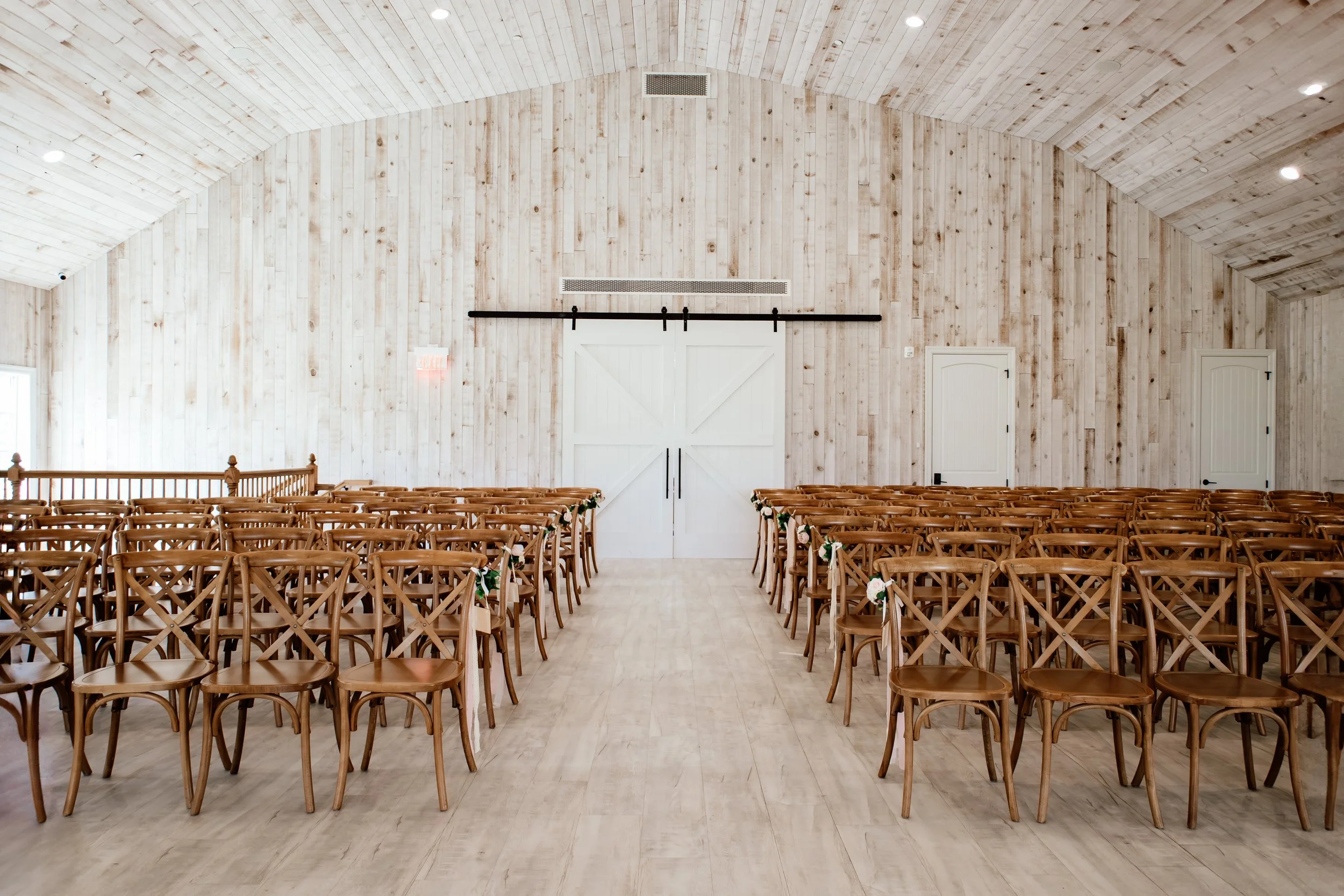 Empty interior wedding chapel with wooden chairs, white barn doors, and wood-paneled walls and ceiling at Laurel Ridge in Sioux Falls SD.