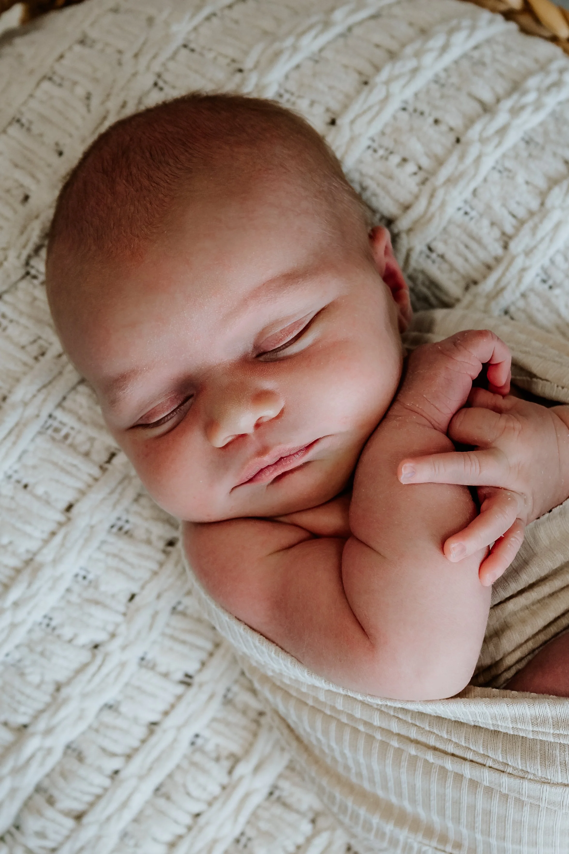 Close-up of a sleeping baby with hands clasped peacefully, lying on a textured, cream-colored blanket at The White Space Studio in Sioux Falls, South Dakota.