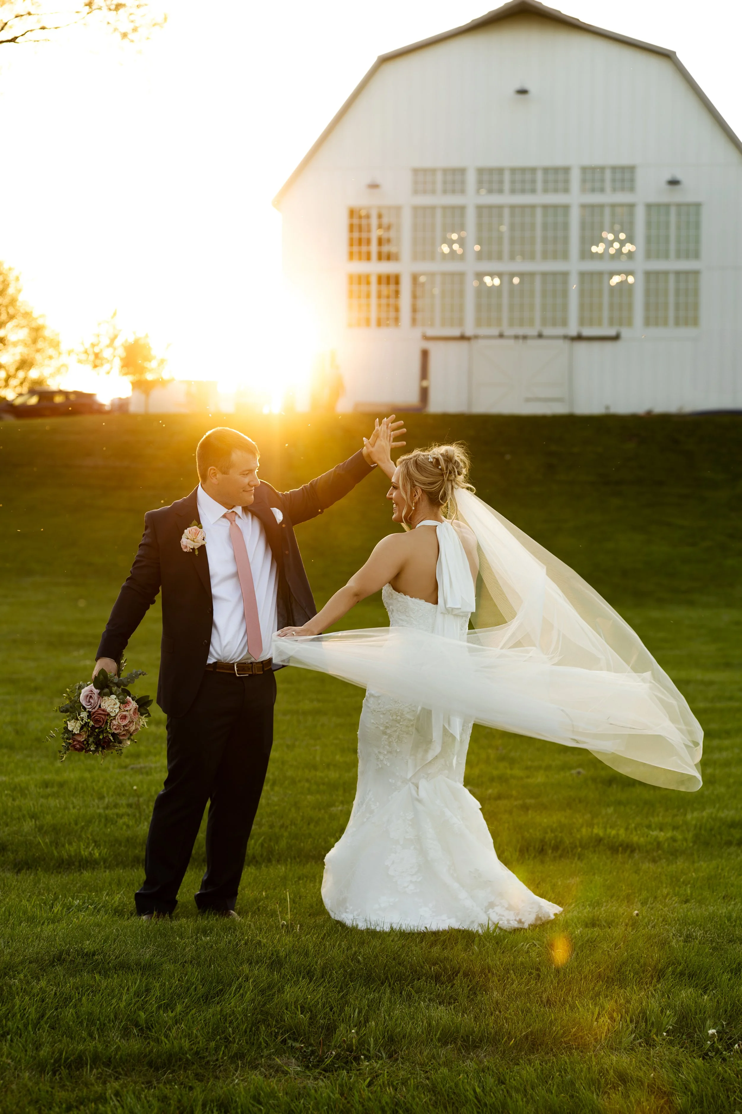A newlywed couple dancing outdoors on a grassy field during sunset, with a large white barn in the background atLaurel Ridge in Sioux Falls, South Dakota.