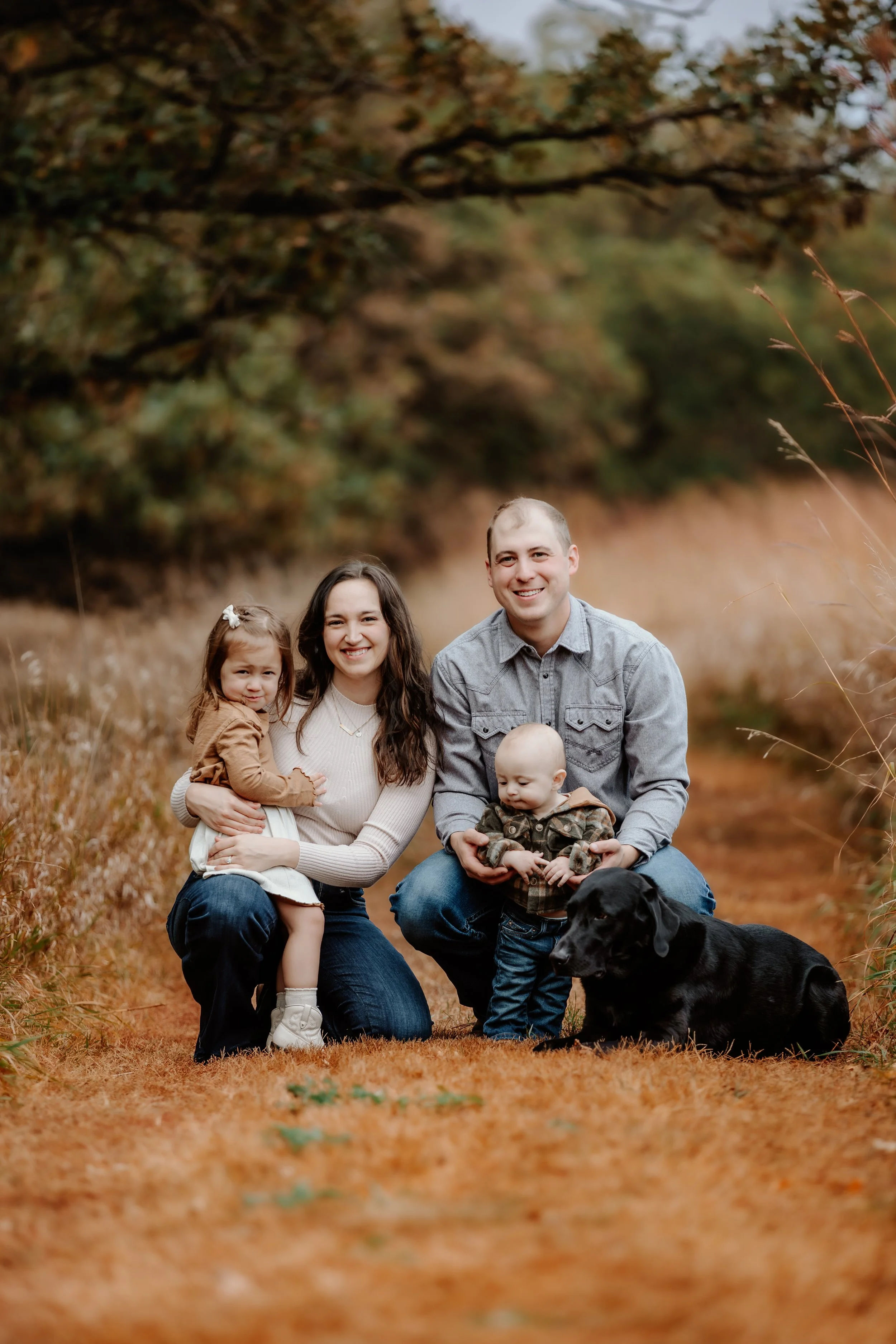 A family of four and a dog posing outdoors in a fall setting with orange leaves and trees in the background  in Sioux Falls, South Dakota at Good Earth State Park.