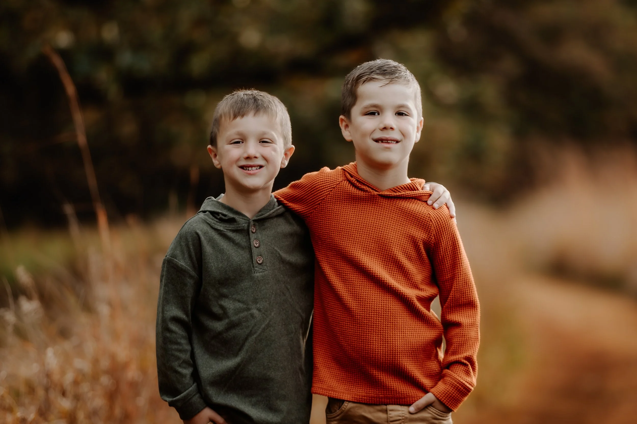 Two boys standing outdoors in a natural setting, smiling and posing together. One has his arm around the other's shoulder in Sioux Falls, South Dakota at Good Earth State Park.